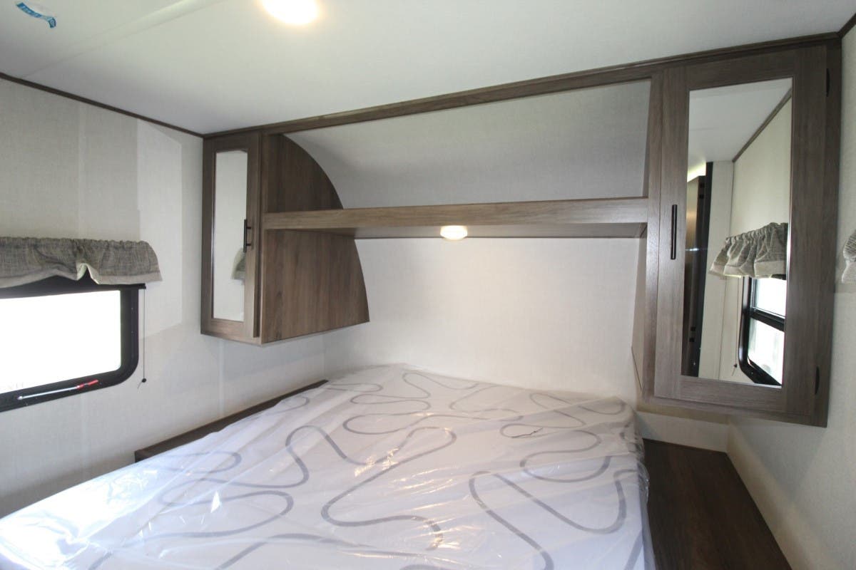 RV rental bedroom showcasing a fresh bed, mirrored overhead cabinets, open shelving, and a window for natural light.. Prime Time Avenger 2021