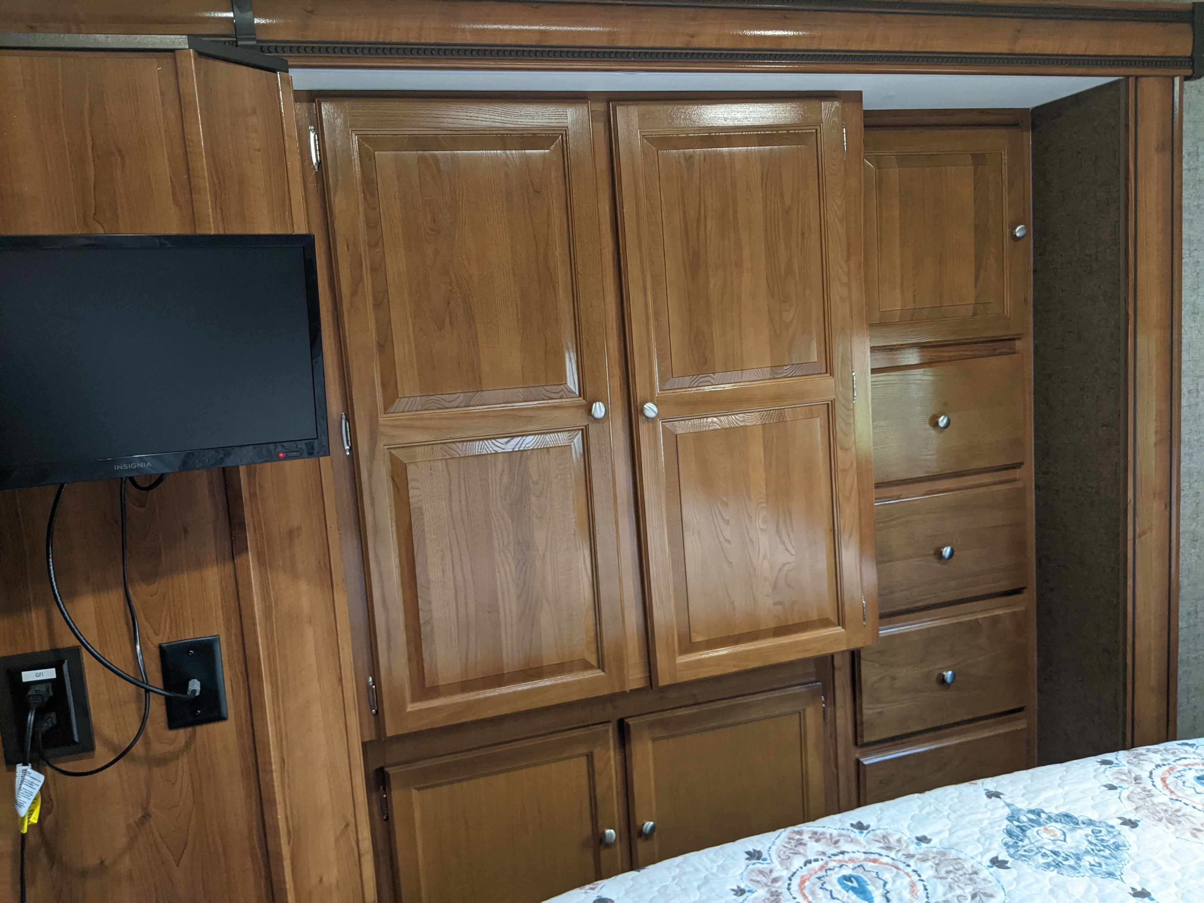 Detailed view of an RV rental bedroom showing wood cabinets, pull-out drawers, and a mounted TV for compact living.. Coachmen Leprechaun 2018