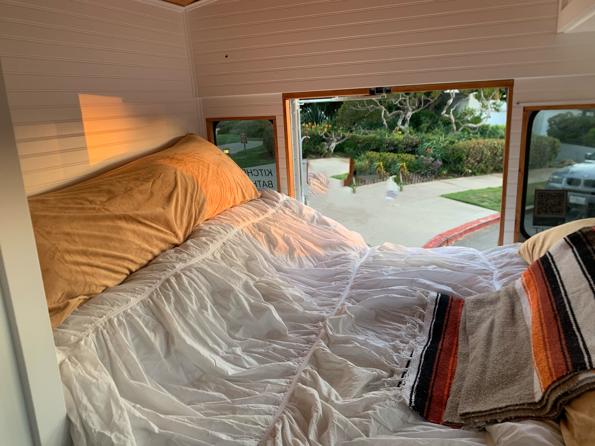 Cozy RV rental interior shows a bed with a view of lush greenery outside the window, bathed in sunlight.. Chevrolet Express 2012