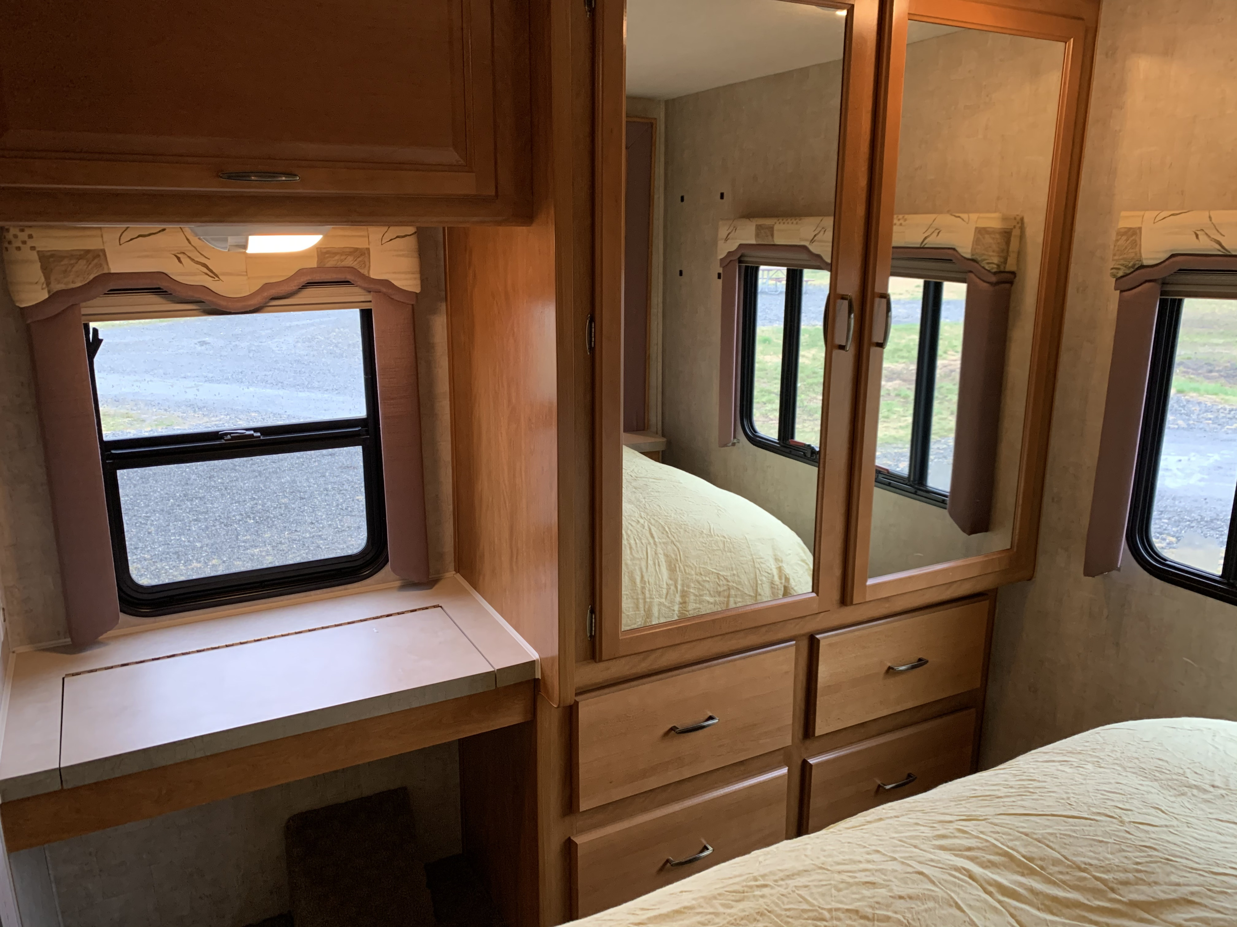 RV rental bedroom featuring a bed, mirrored wardrobe, and desk. Comfortable motorhome interior with windows offering outdoor views.. Tioga M-30u Ford 2005