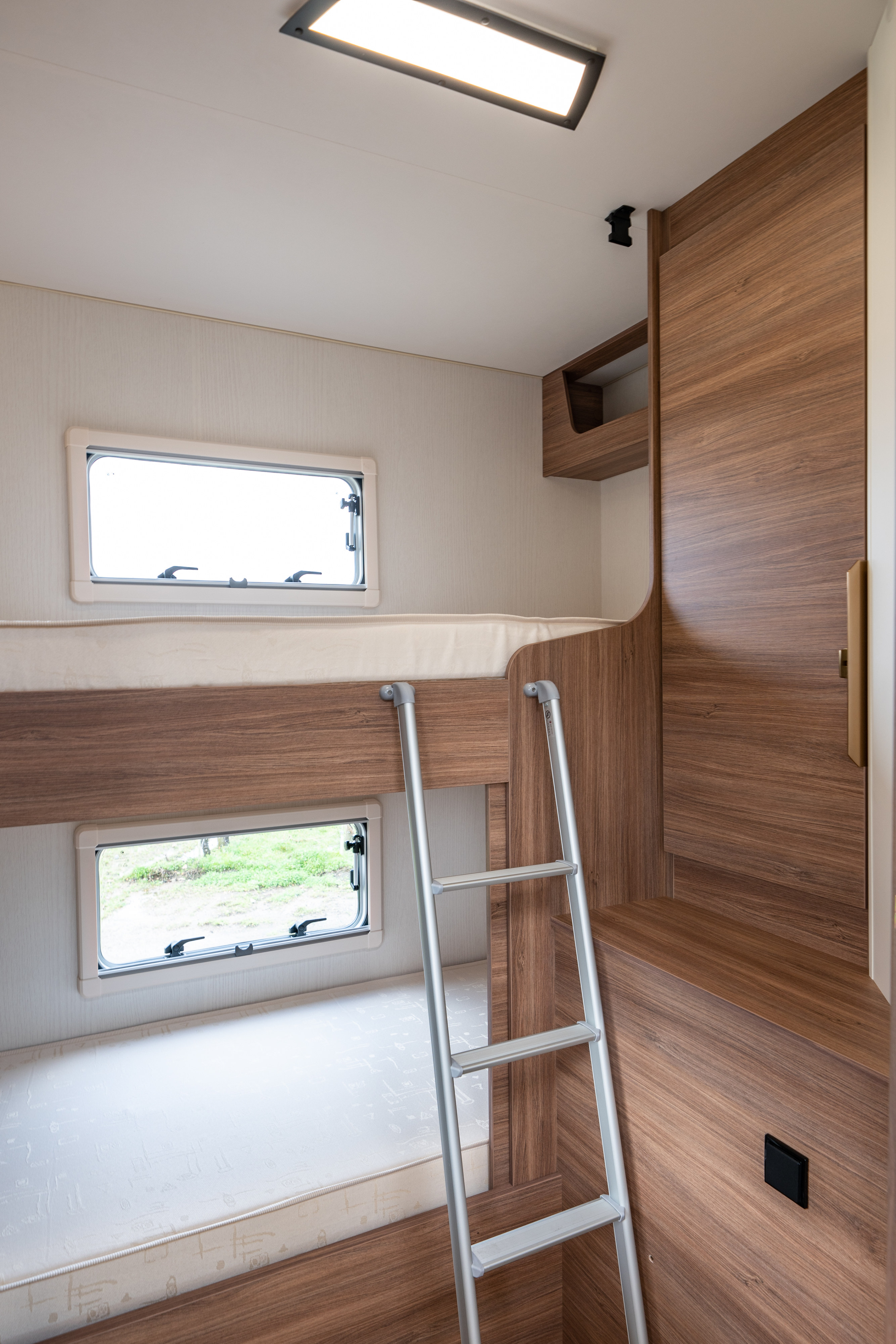 Inside an RV rental: view of bunk beds, ladder, windows, and wooden storage/wardrobe. Bright, functional interior.. Pilote P690S EXPRESSION 2025
