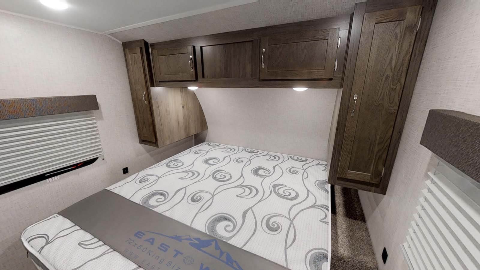 RV rental bedroom featuring a king bed with patterned mattress, overhead storage, and window blinds. Compact & functional.. East to West Della Terra 2021