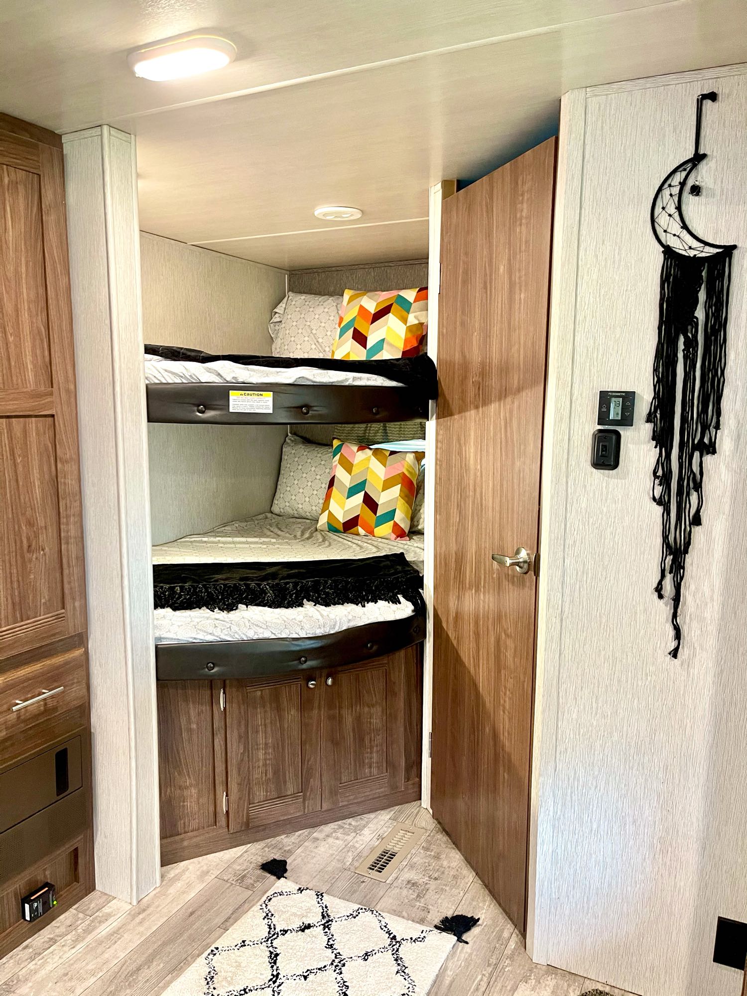 View of an RV rental's cozy bunk bed setup with colorful pillows, a wooden door, and unique moon decor inside.. Heartland Pioneer 2018