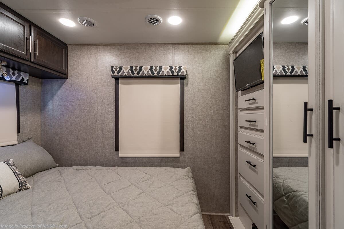 Modern RV rental bedroom featuring a cozy bed, overhead cabinets, a dresser with TV, and mirrored closet.. Entegra Coach Other 2021