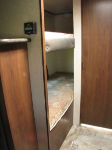 View inside an RV rental showing a compact bunk bed area with two sleeping surfaces. A thermostat is mounted on the adjacent wall.. Jayco Jay Flight 154BH 2016