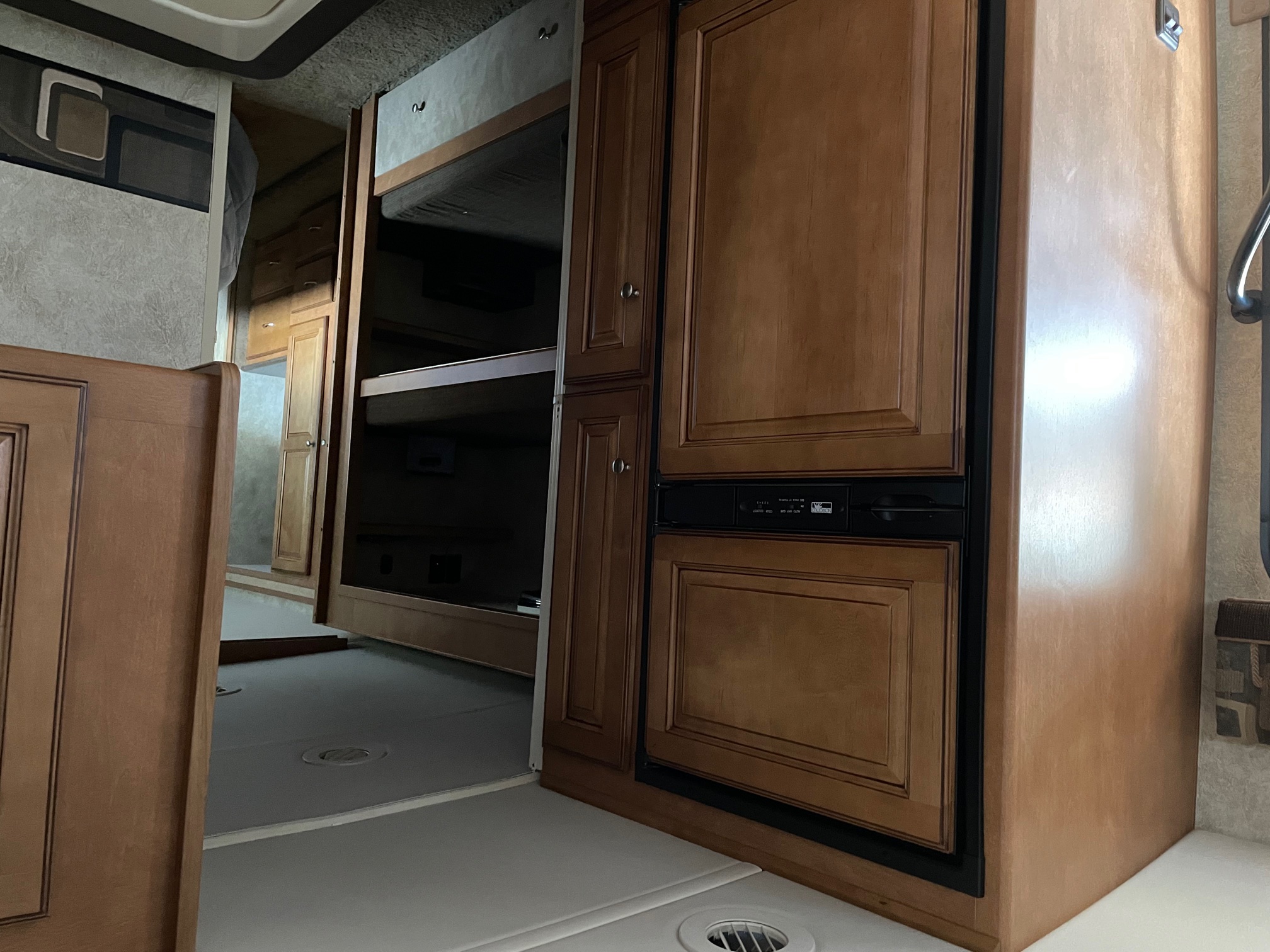RV rental interior showing the kitchen area with wooden cabinets, a built-in refrigerator, and bunk beds in the back.. Itasca Sunstar 2012
