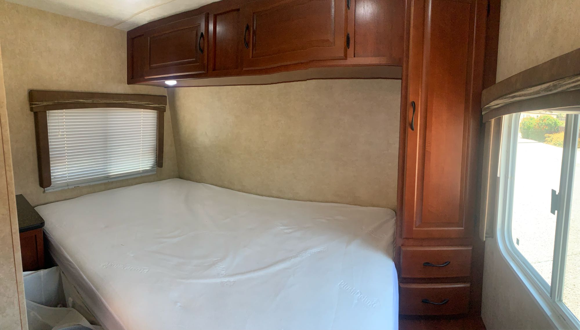 Interior of an RV rental: a compact bedroom with a white mattress, wooden overhead cabinets, and a window with blinds.. Forest River Other 2013