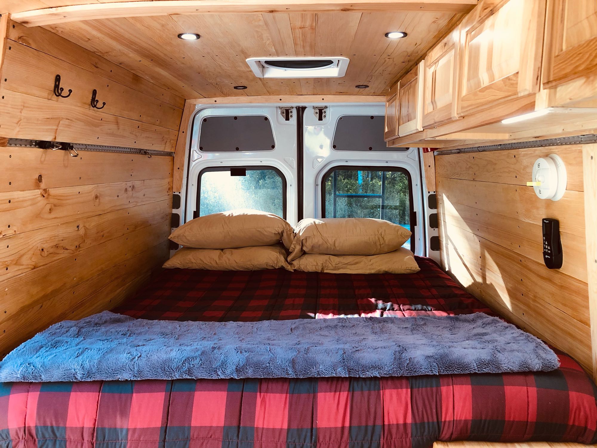 Cozy RV rental bedroom featuring wood interior, plaid bedding, overhead cabinets, and essential safety features for comfortable travel.. Mercedes Sprinter 2014