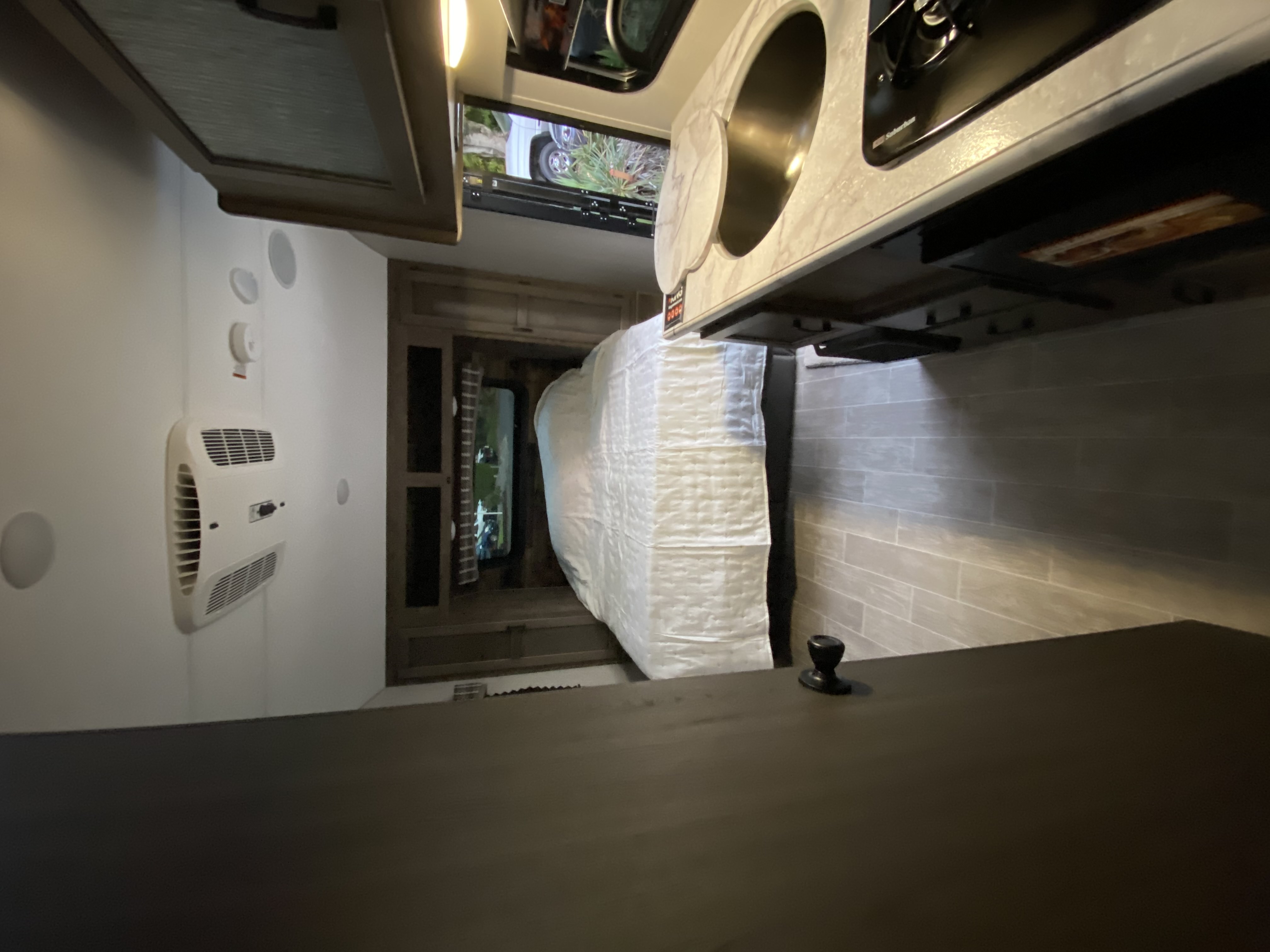 Compact RV rental interior featuring a bedroom area with a bed, a kitchen with a sink and stovetop, and an AC unit on the wall.. Sonic Lite 2021