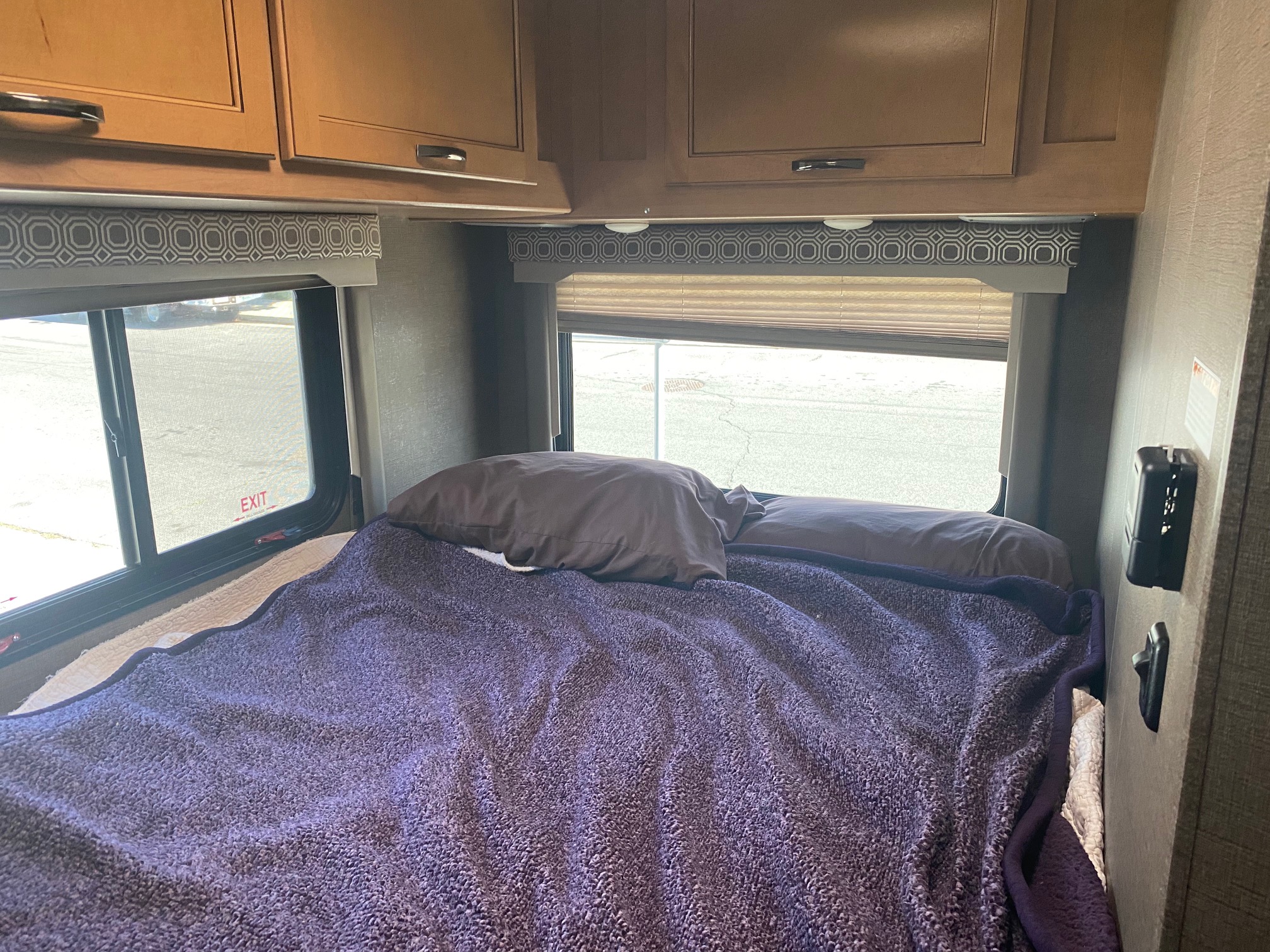 RV rental cozy bedroom showing a purple blanket, pillows, light wood cabinets, and two large windows with valances.. Thor 22E 2017