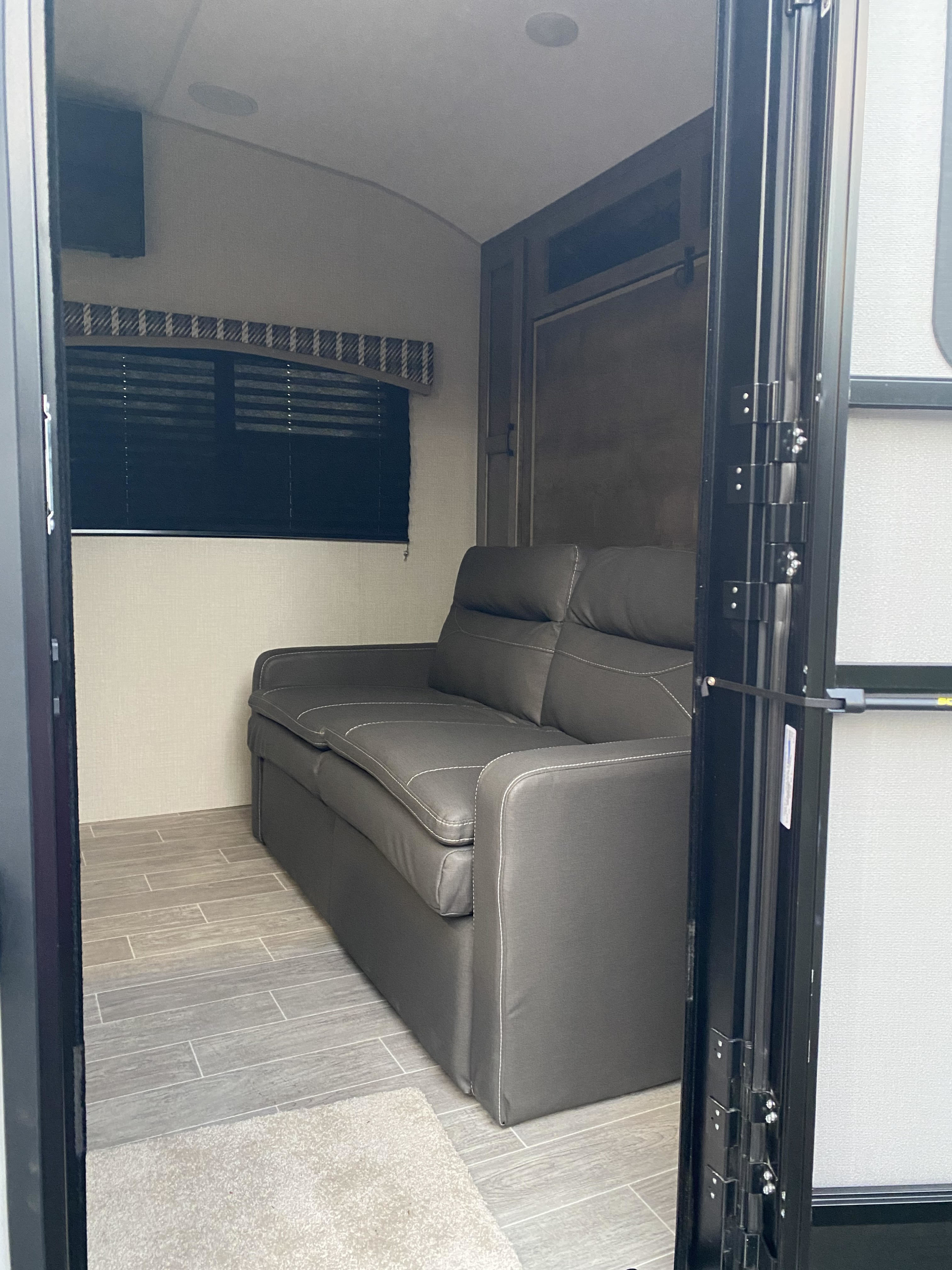 Interior view of an RV rental showing a gray sofa, wall-mounted TV, window with blind, and wood-look tile floor.. Sonic Lite 2021