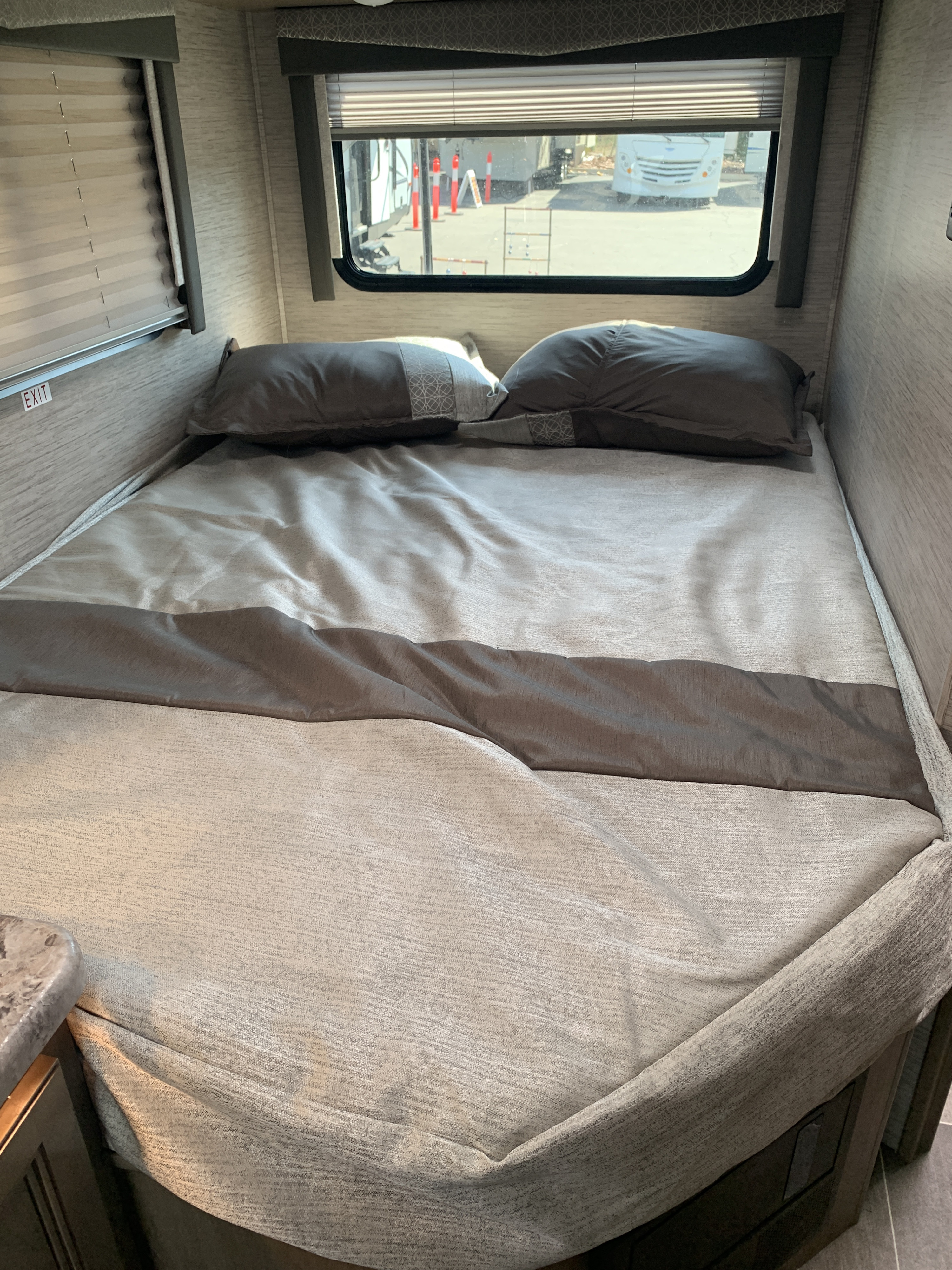 Inside an RV rental bedroom: a cozy bed with pillows, comforter, and windows offering a view outside.. Thor Motor Coach Chateau 2022