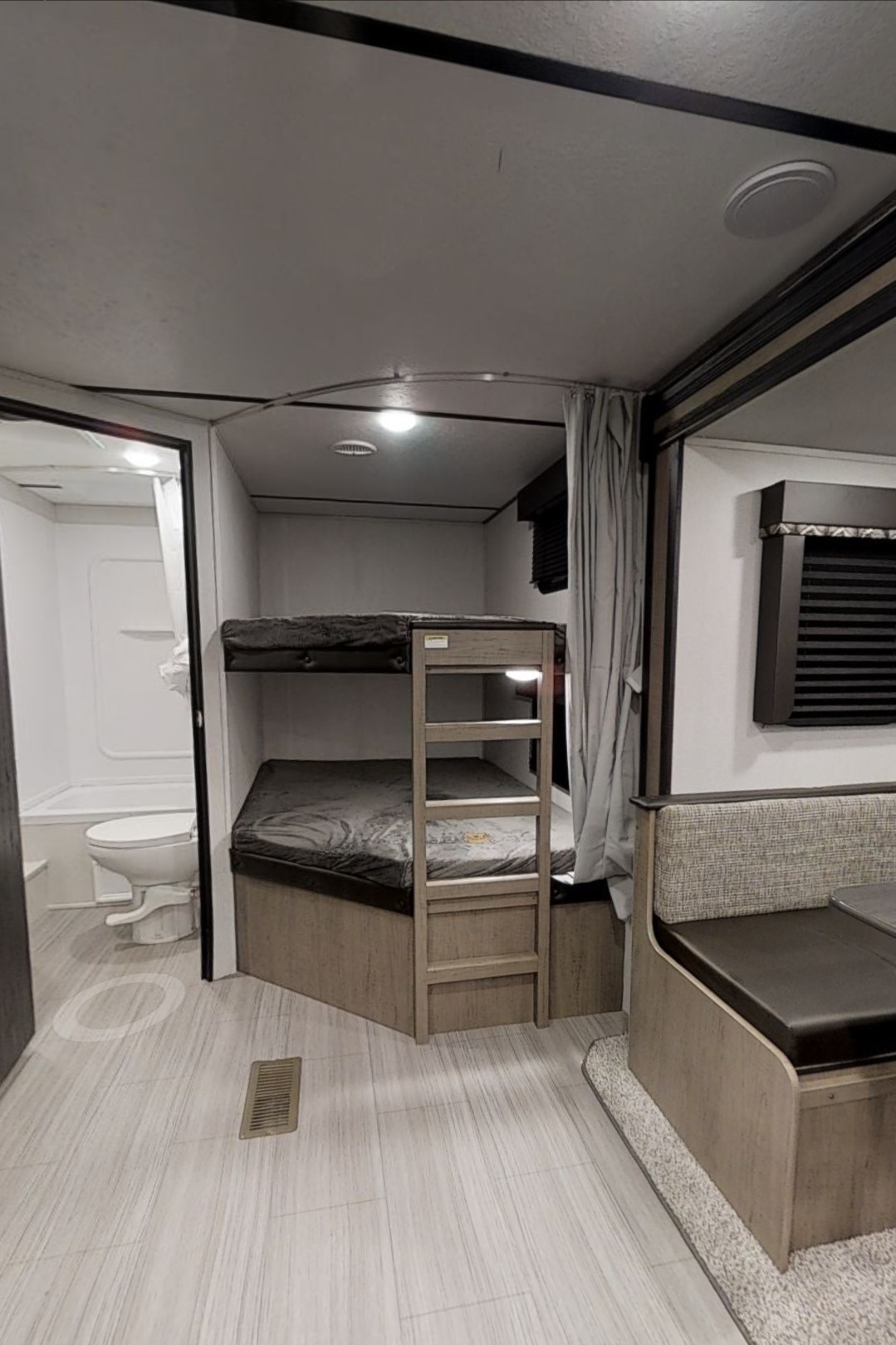 Interior view of an RV rental showing bunk beds, a small bathroom with a toilet/tub, and a cozy dining area.. Keystone Hideout 2021