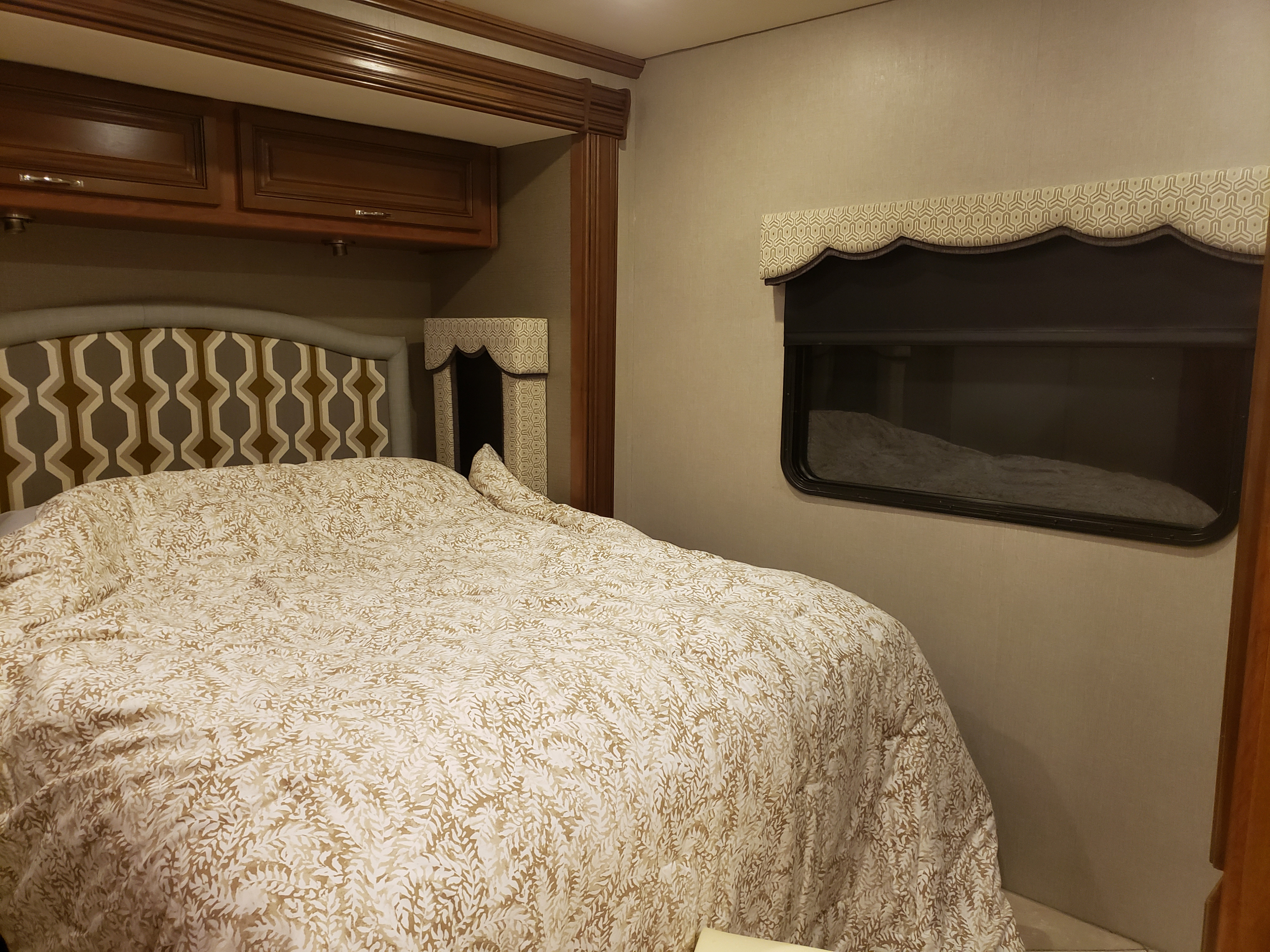 RV rental bedroom showcasing wood cabinets, a geometric headboard, and a cozy bed with leaf-patterned comforter.. Holiday Rambler Vacationer 2015