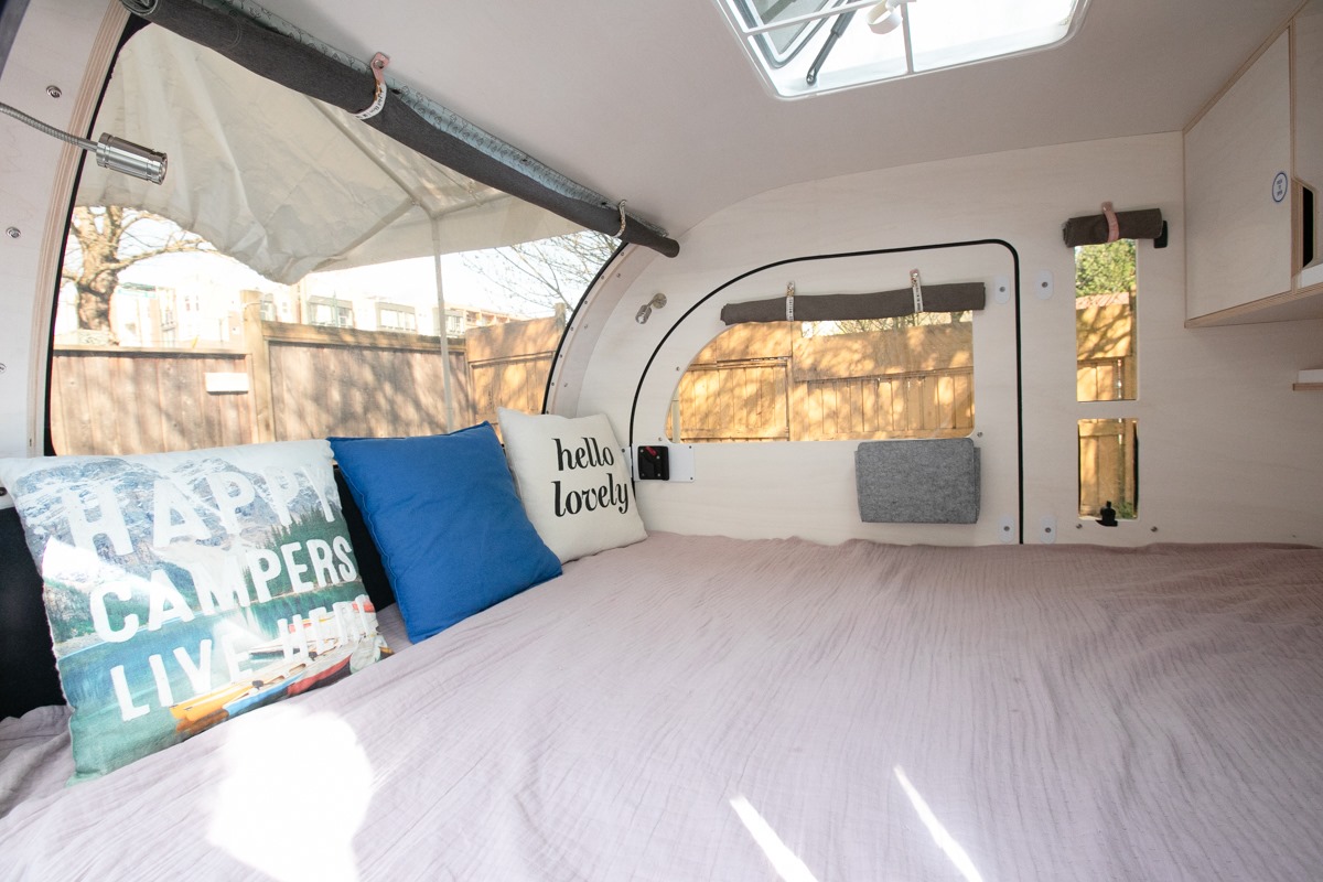 Cozy RV rental interior with a comfy bed, decorative pillows, and large scenic windows.. Droplet Teardrop 2020