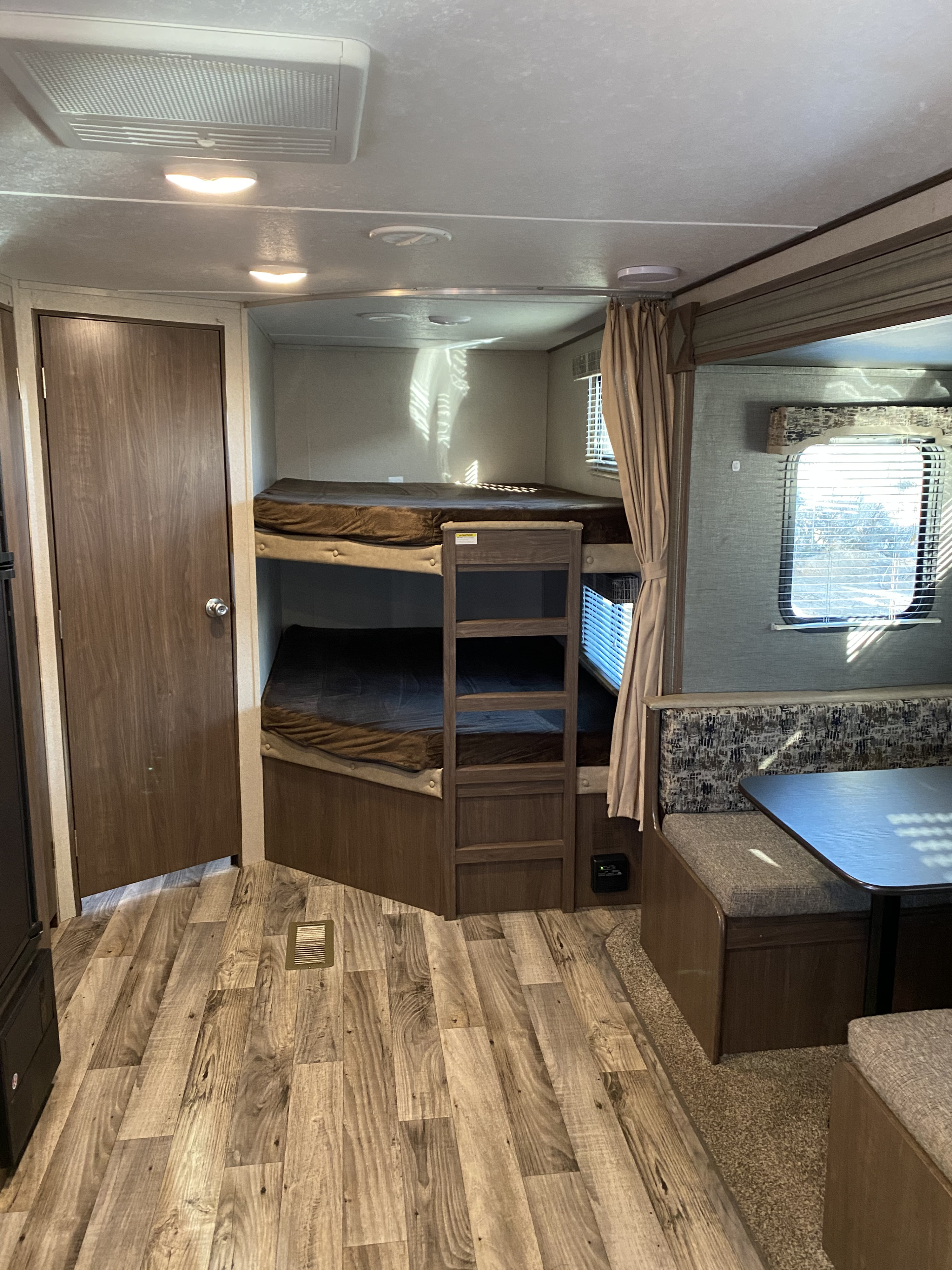 An RV rental interior showing bunk beds, a dinette with table, and wood-look flooring, lit by natural light.. Keystone RV Hideout 2019