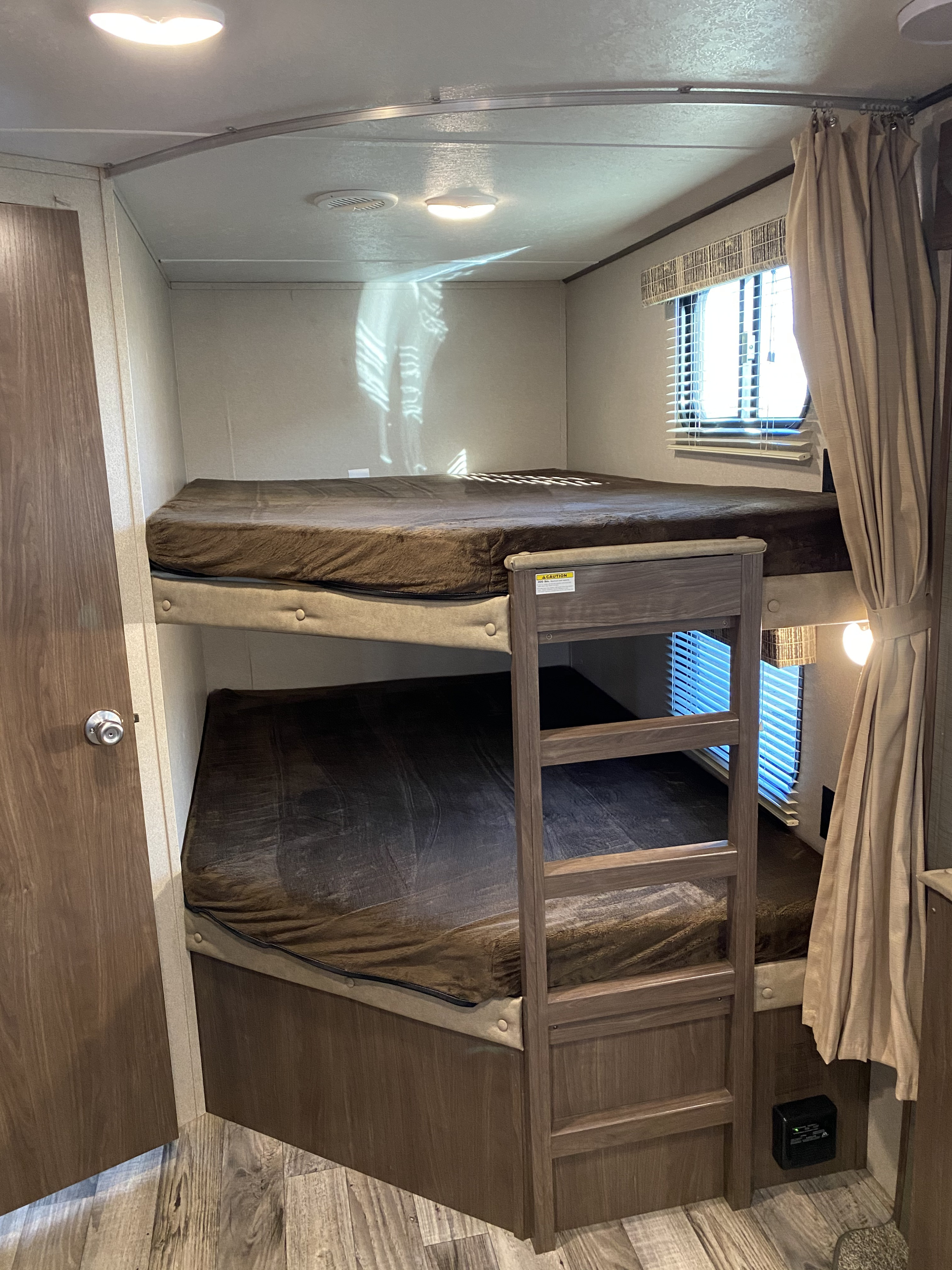 Compact bunk beds in an RV rental, featuring cozy brown blankets, a wooden ladder, and a window with blinds.. Keystone RV Hideout 2019