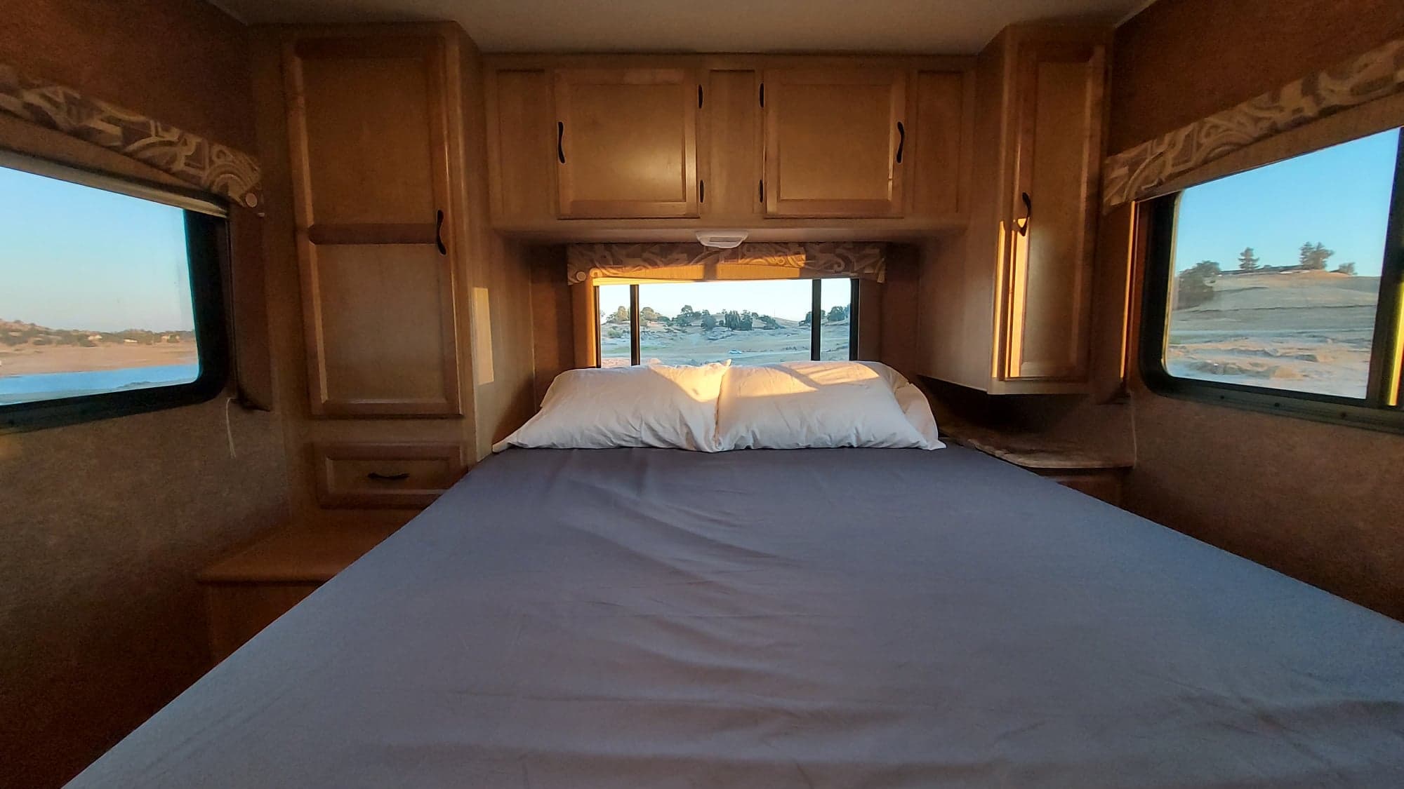 Inside an RV rental bedroom with a comfy bed, wooden cabinets, and large windows revealing diverse outdoor scenery.. Chevrolet Forester 2014