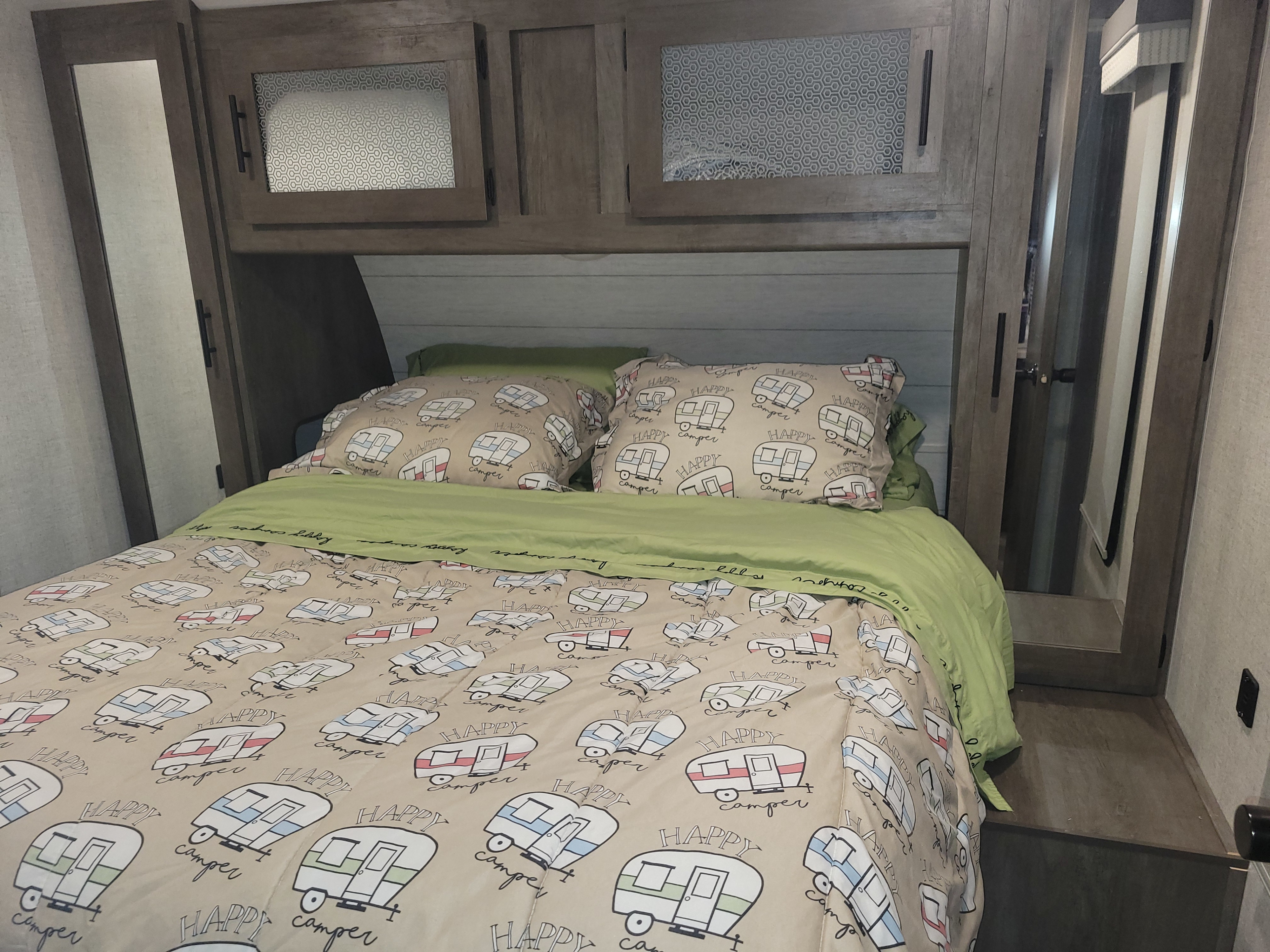 Step into comfort! This RV rental bedroom features fun 'Happy Camper' bedding and convenient overhead storage.. Forest River Salem 2021