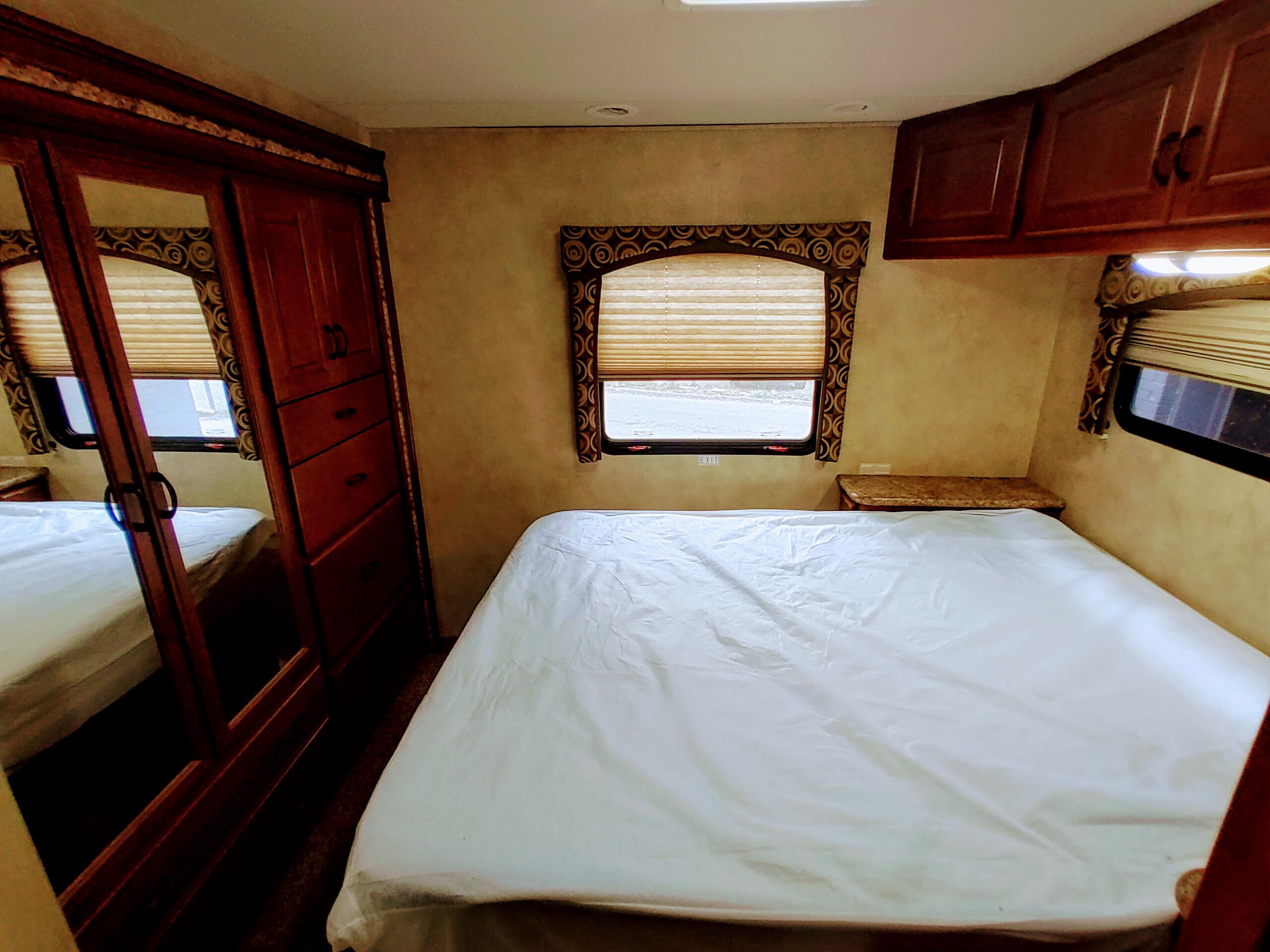 Spacious RV rental bedroom featuring a large bed, mirrored wardrobe, window, and overhead cabinets for a comfortable stay.. Thor Motor Coach Hurricane 2011