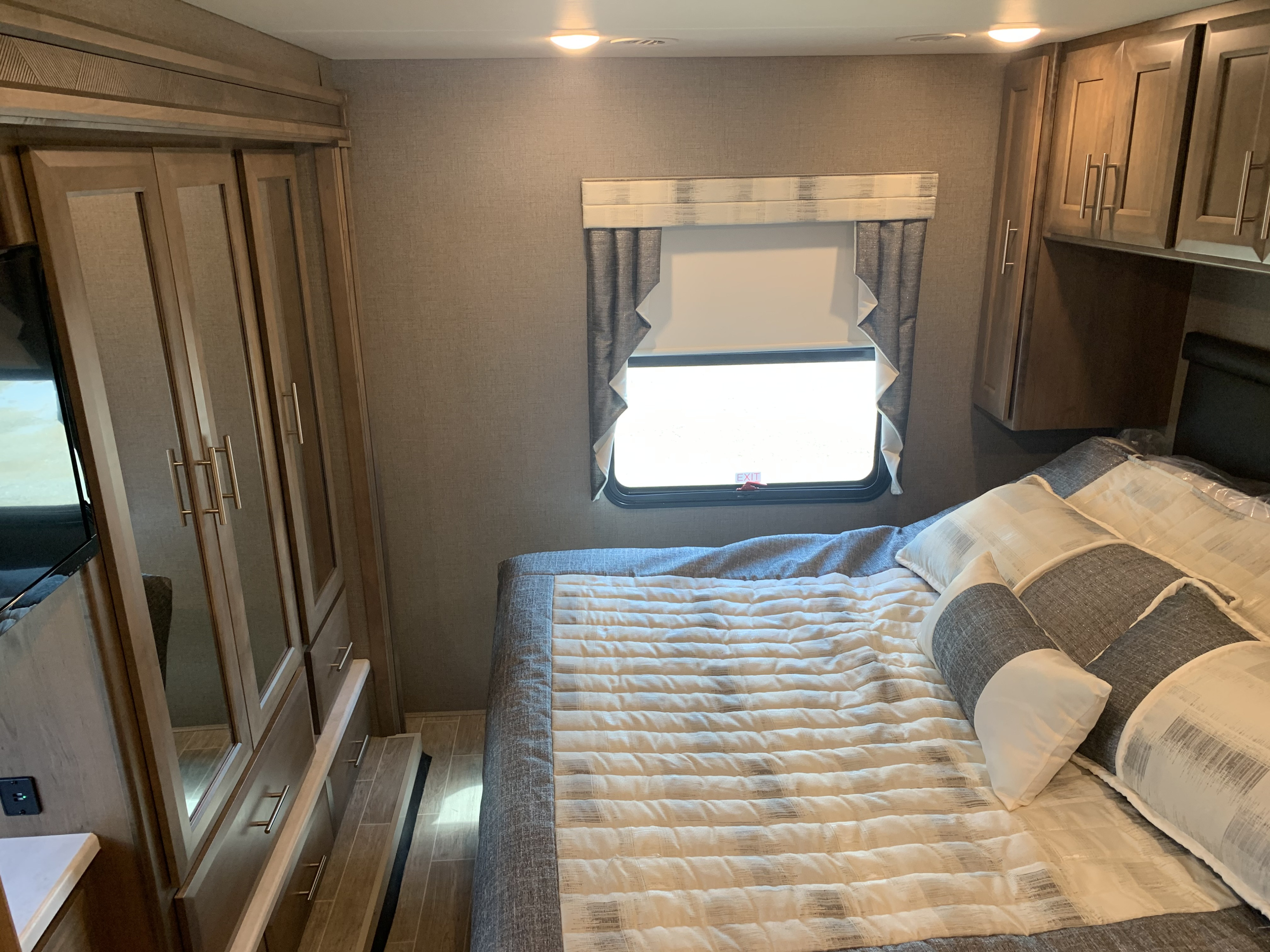 Cozy RV rental bedroom featuring a striped bed, wood cabinets, and a window. A comfortable and well-appointed space.. Thor Motor Coach Miramar 2021