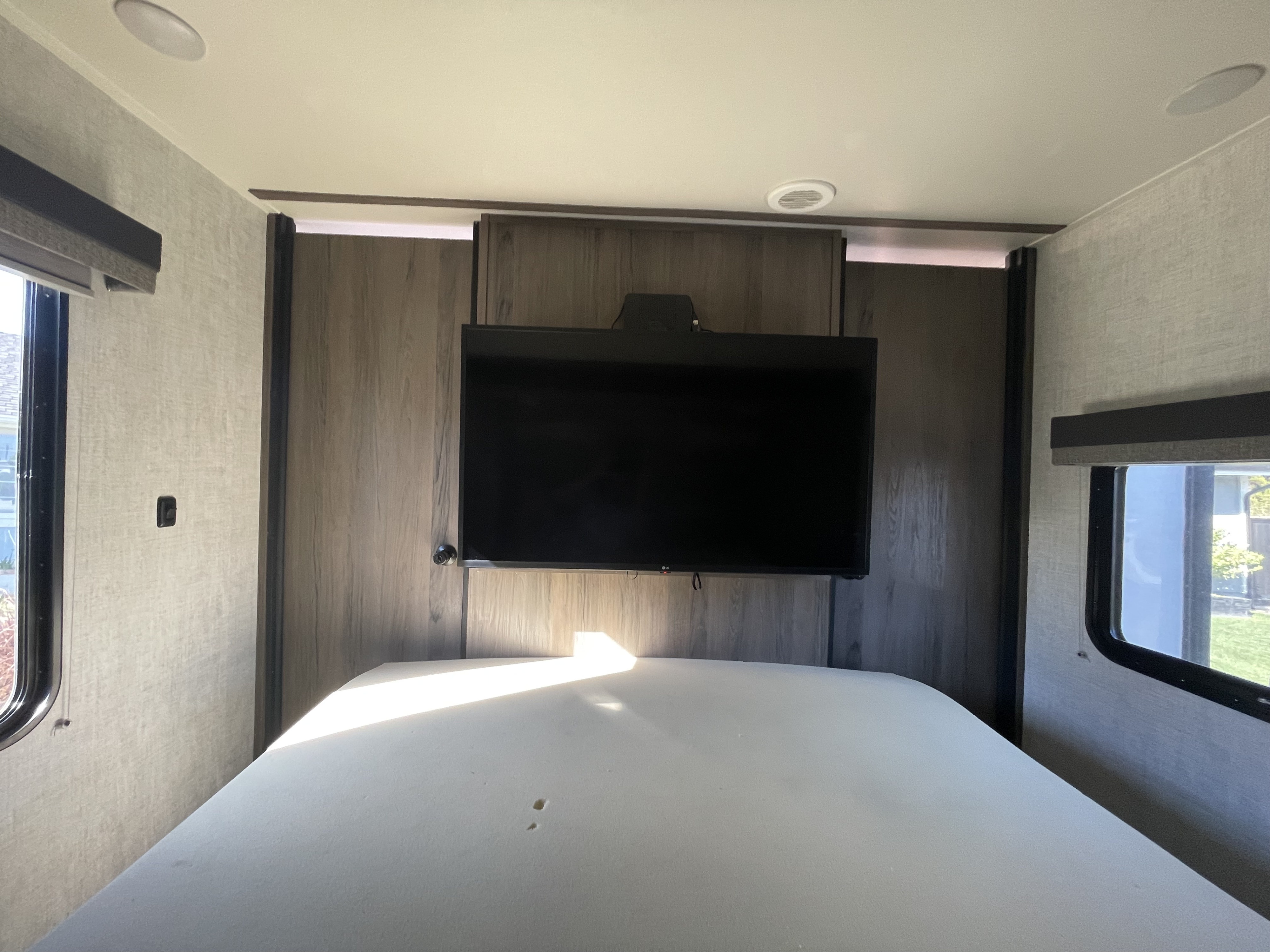 Modern RV rental bedroom featuring a bed, mounted TV, and sunlit windows, designed for comfortable rest.. Gulf Stream Amerilite 2021
