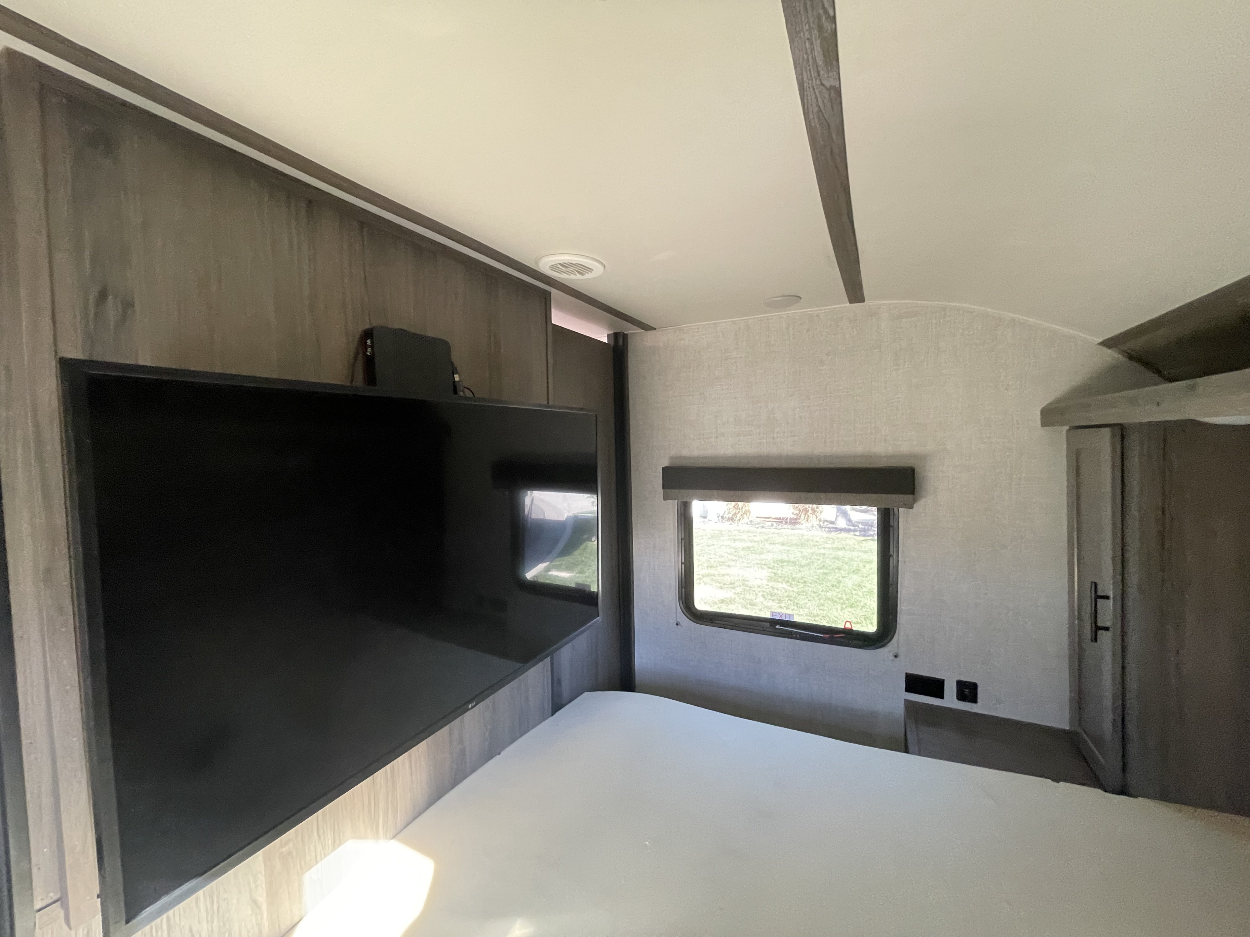 Inside an RV rental bedroom: flat-screen TV mounted above a clean bed, window with outdoor view, and closet space.. Gulf Stream Amerilite 2021