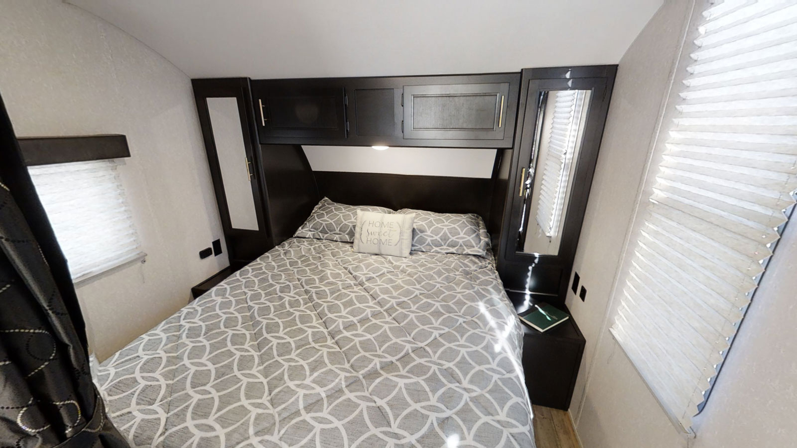 Inviting RV rental bedroom with patterned bedding, overhead storage, and bedside amenities.. Forest River Cherokee Grey Wolf 2021