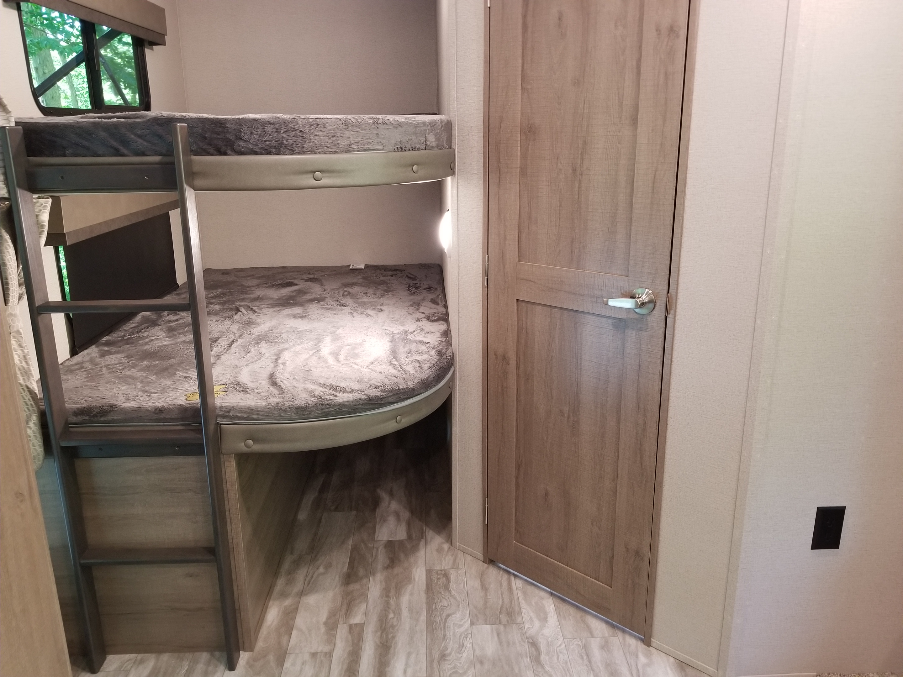Inside this RV rental: comfortable two-tier bunk beds with a ladder, a window overlooking trees, and a light-colored wooden door.. Grand Design Imagine 2021
