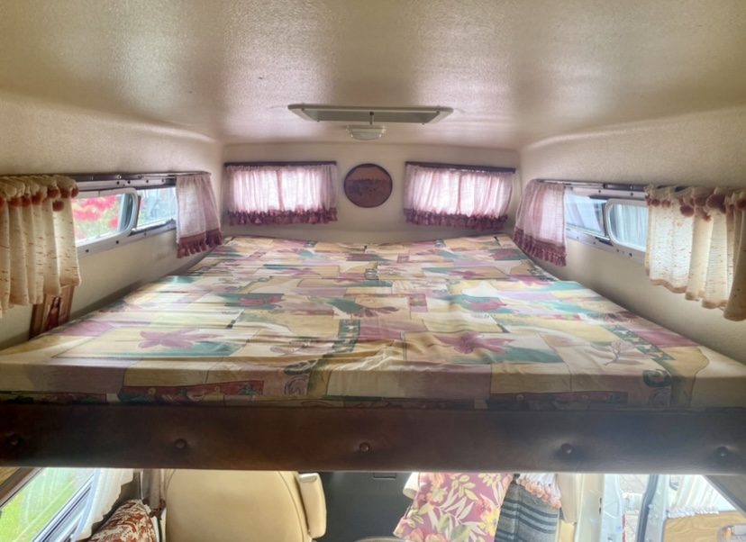 Spacious overhead sleeping area in this RV rental, with a colorful comforter, windows, and curtains.. Frontier Other 1979