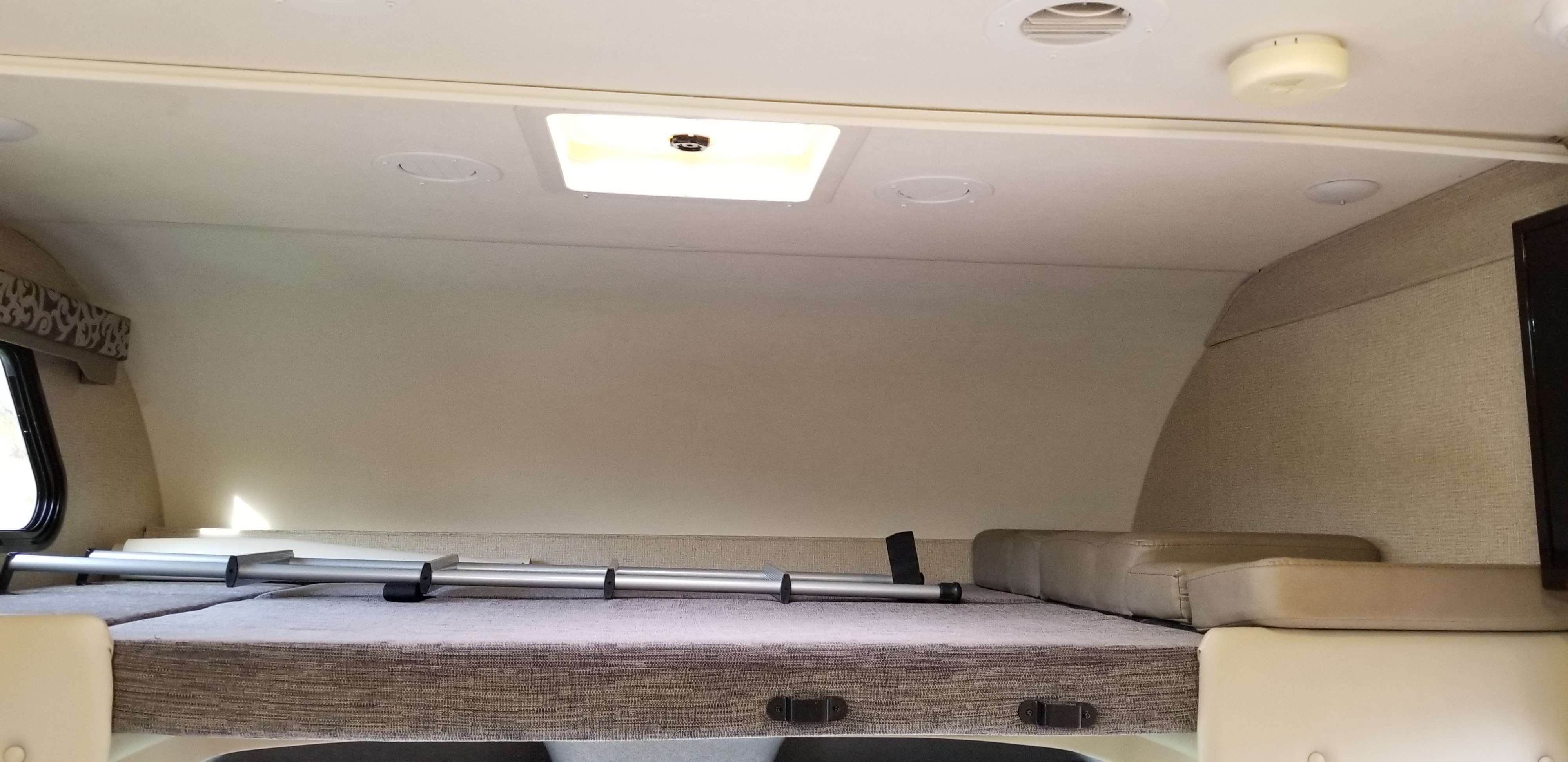 Inside an RV rental: a cozy cab-over bunk bed with overhead lighting, a window, and neutral wall textures.. Mercedes Benz Four Winds 2018