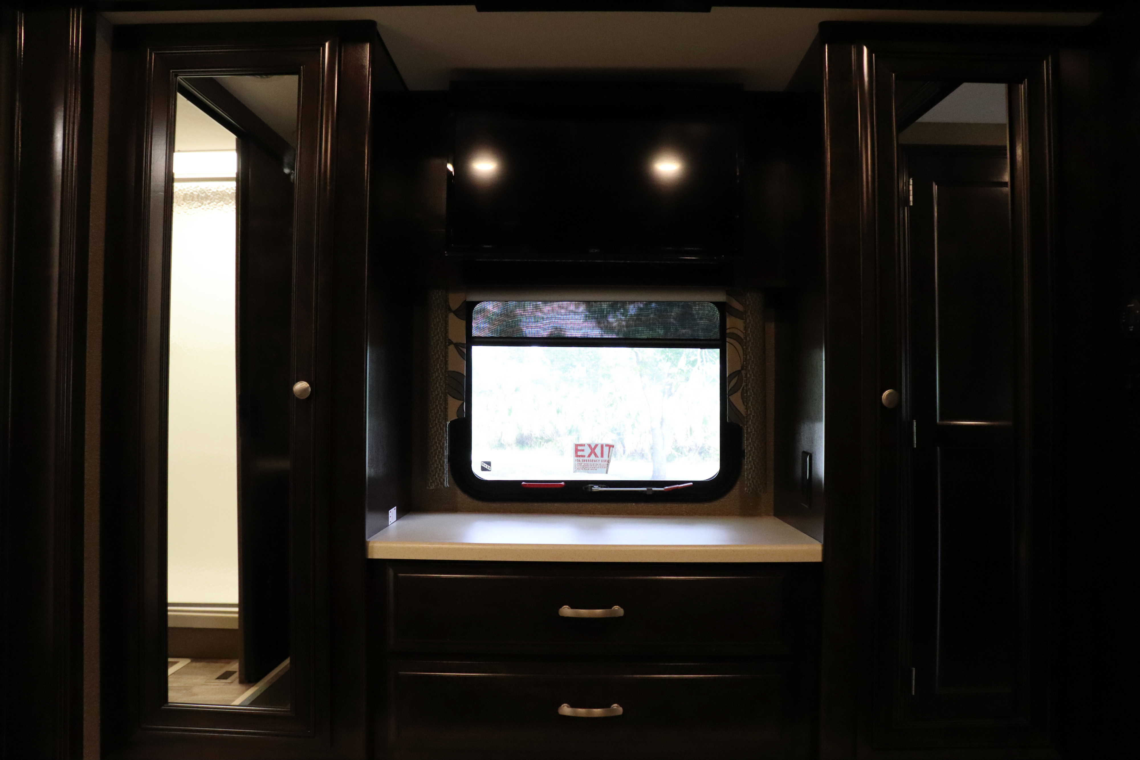RV rental bedroom interior with dark wood cabinets, mirror, TV, window with view, and drawers.. Thor Motor Coach Palazzo 2016