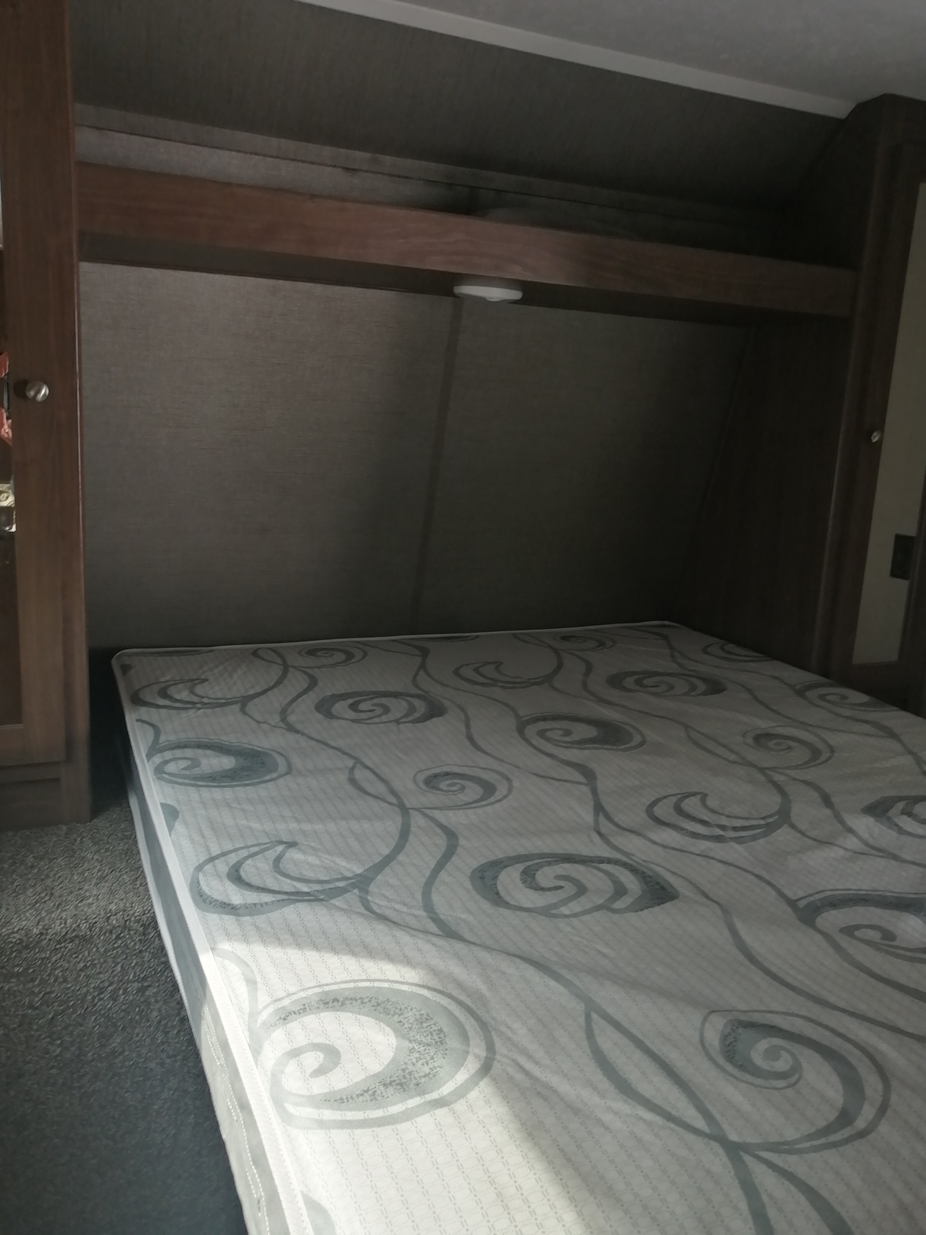 RV rental bedroom: patterned mattress, dark fabric walls, wooden trim, overhead light, and carpeted floor.. Keystone Hideout 2018