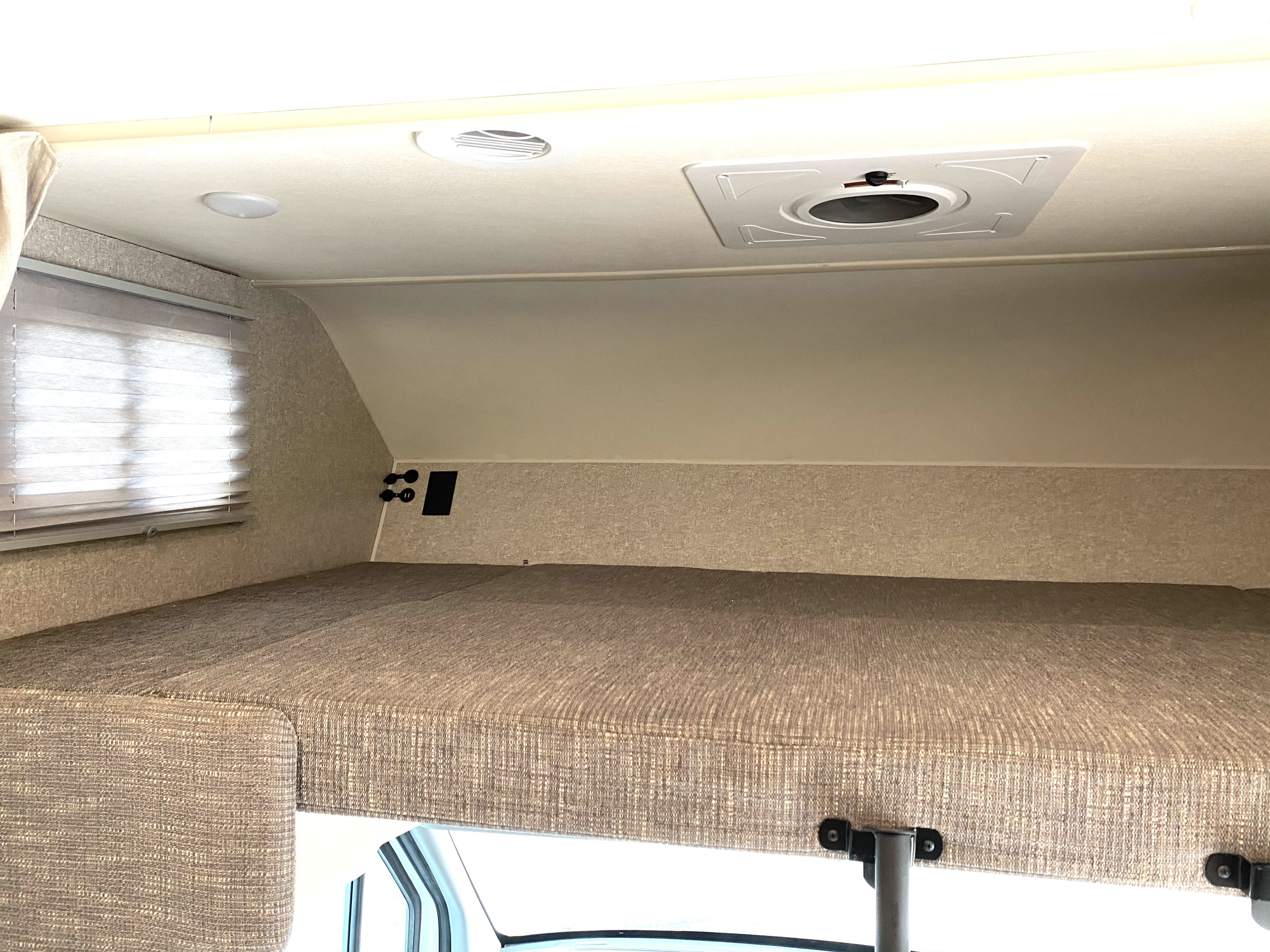 Experience comfortable sleeping in this RV rental's cab-over bunk, featuring a cozy mattress, window blinds, and ceiling lights.. Winnebago Porto 2020