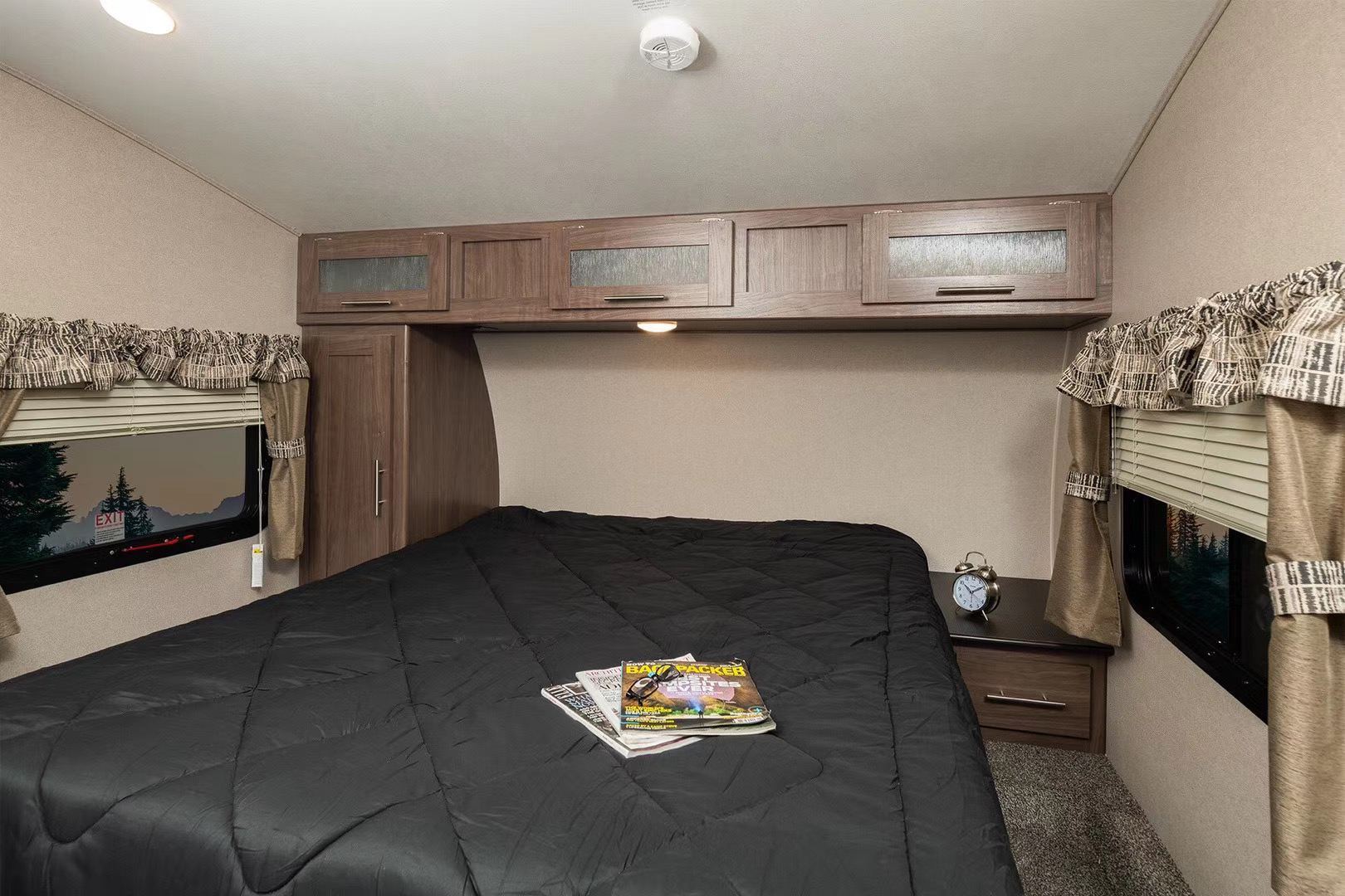 Relax in this cozy RV rental bedroom. Features a large bed, overhead cabinets, and windows with outdoor views.. Keystone RV Hideout LHS 2019