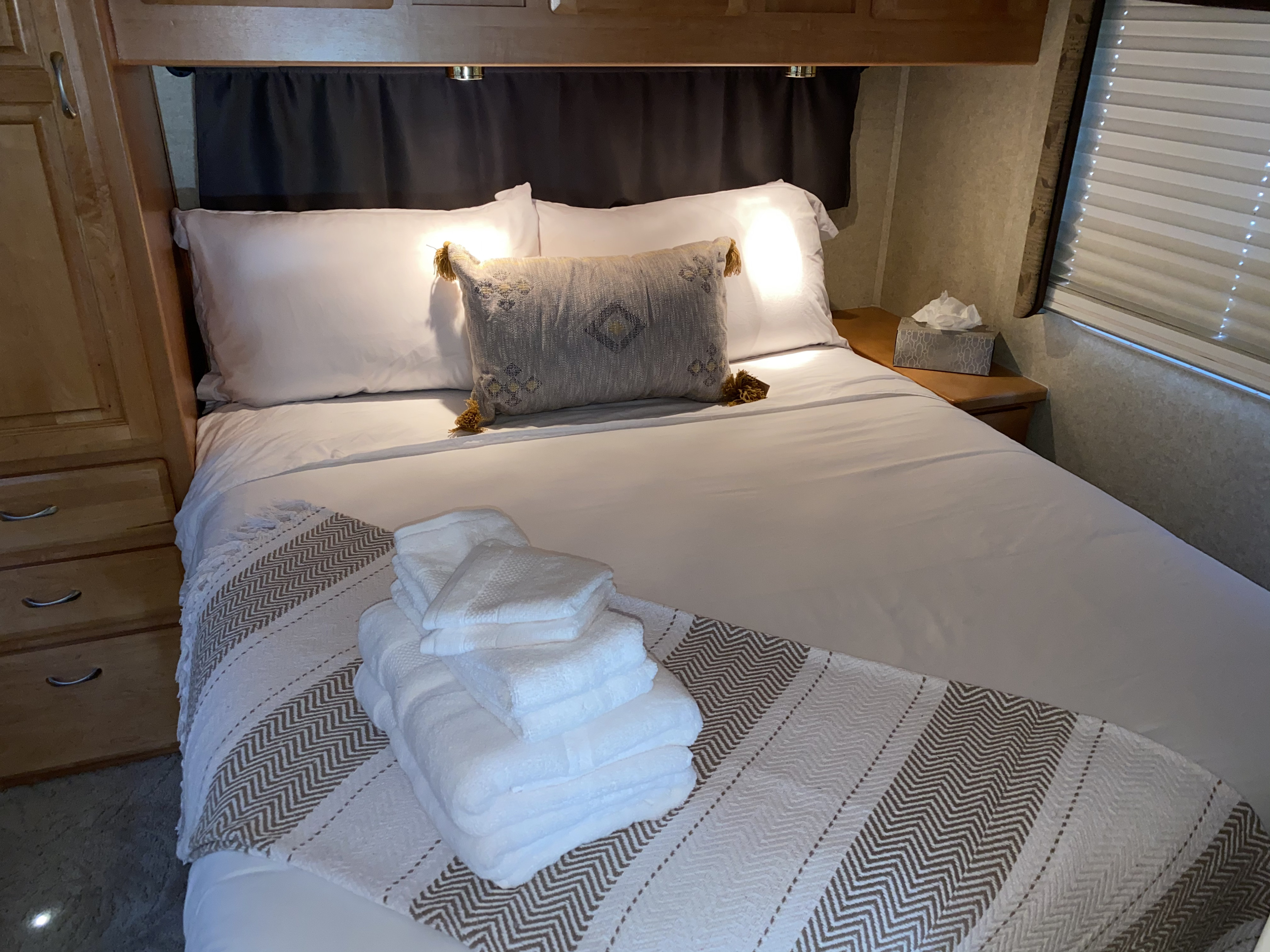 Well-appointed RV rental bedroom with fresh white linens, decorative pillow, folded towels, and functional amenities.. Jayco Granite Ridge 2003