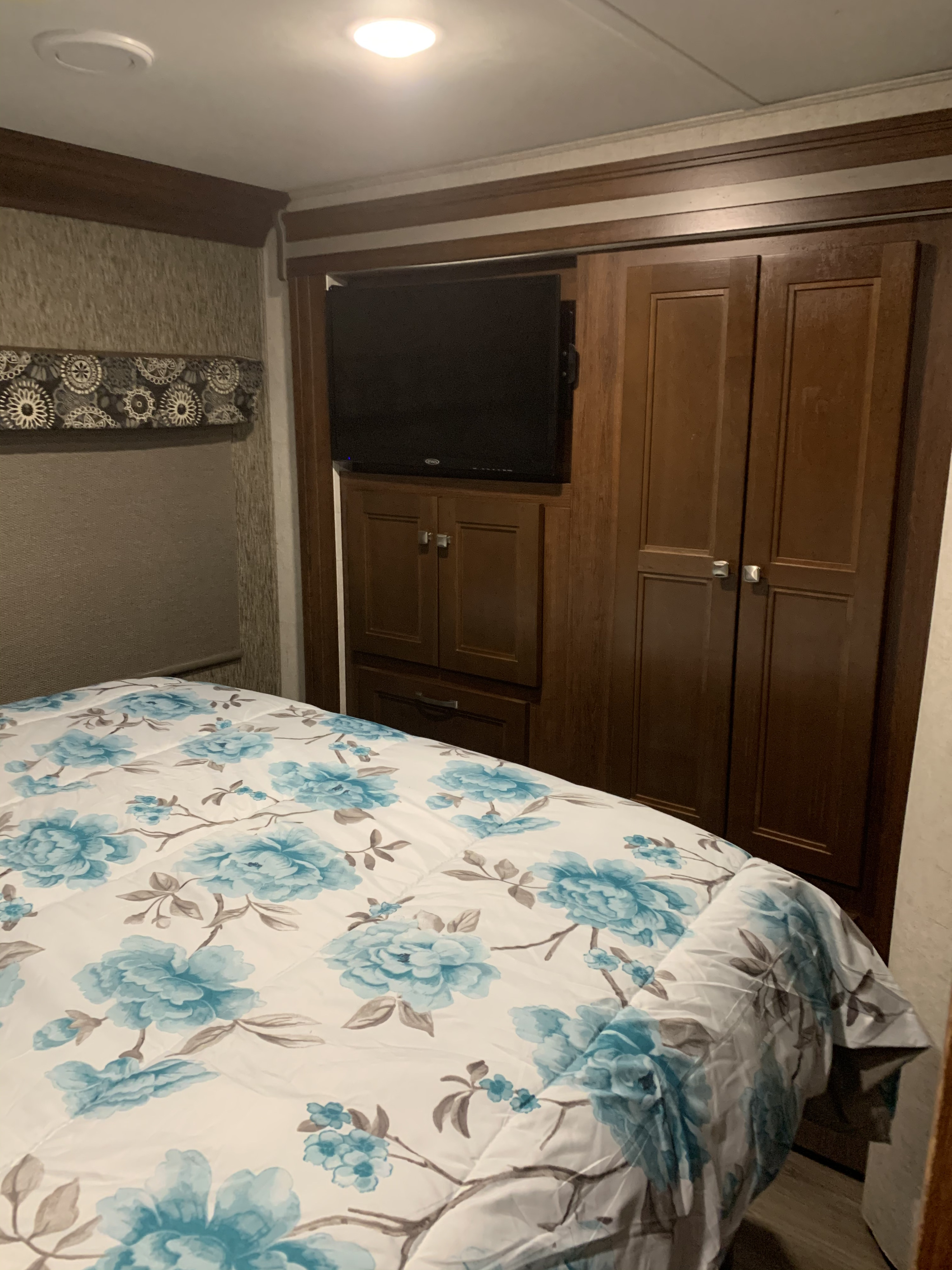 RV rental bedroom: floral bed, wall-mounted TV, and wooden storage cabinets, offering compact comfort.. Ford E450 2018