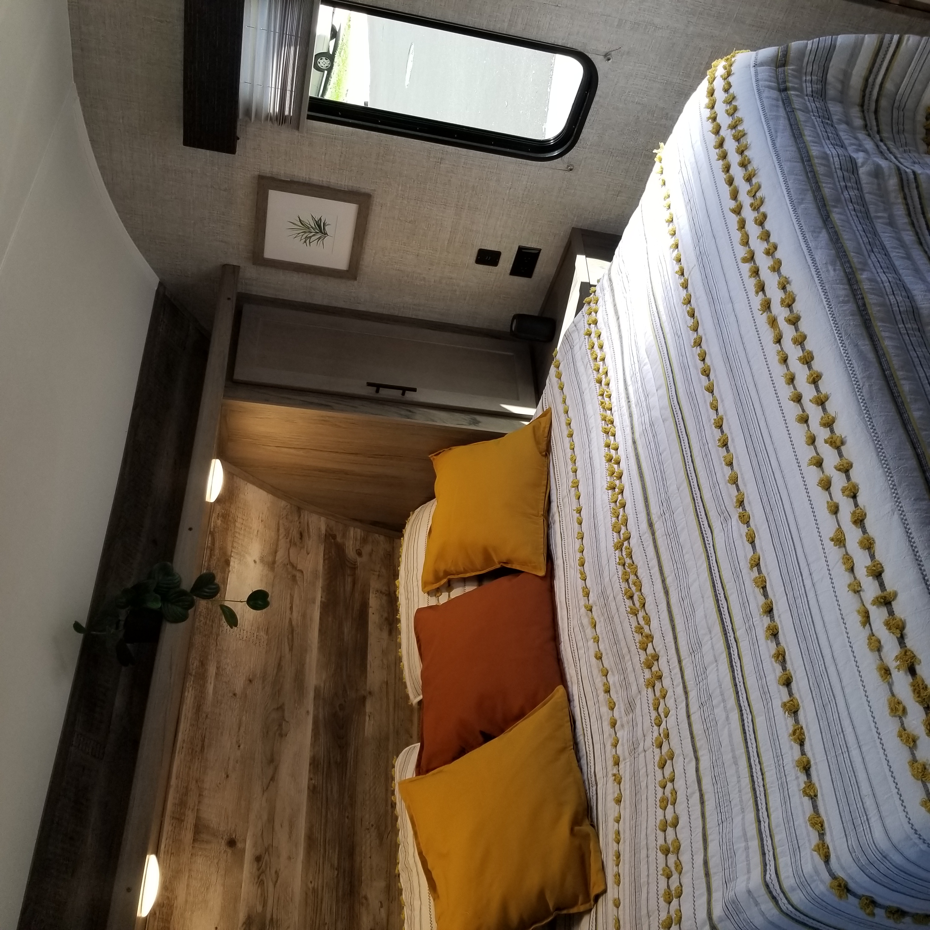 Cozy RV rental bedroom featuring wood paneling, striped bedding with yellow accents, and an overhead window.. Gulf Stream Amerilite 2021