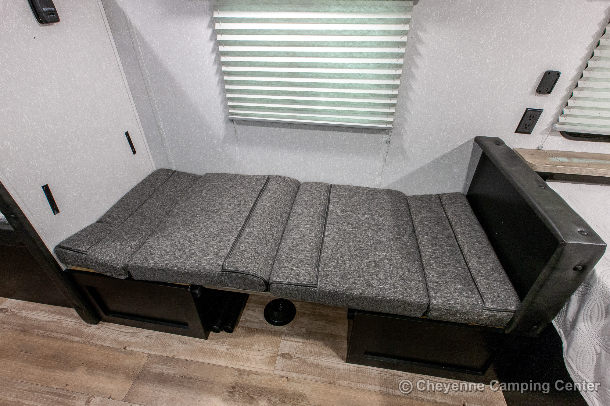 RV rental interior: A gray upholstered bench, ideal for seating or converting to a bed, with wall outlets & a window blind. Perfect for compact living.. Forest River Cherokee Wolf Pup 2021