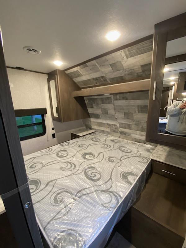 Cozy RV rental bedroom with a new queen mattress still in plastic, stylish wood accents, and integrated storage.. Other Other 2021