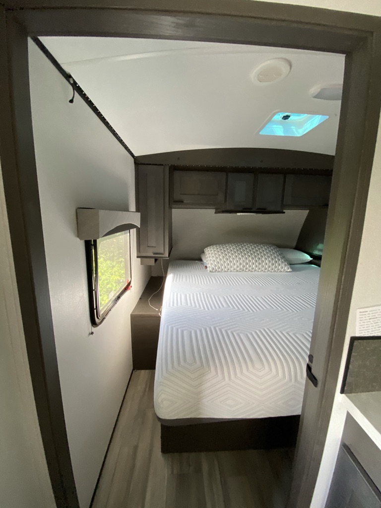 Inside a modern RV rental bedroom: a comfortable bed, overhead cabinets, and a window for natural light, framed by a doorway.. Cruiser Rv Corp Cruiser 2021