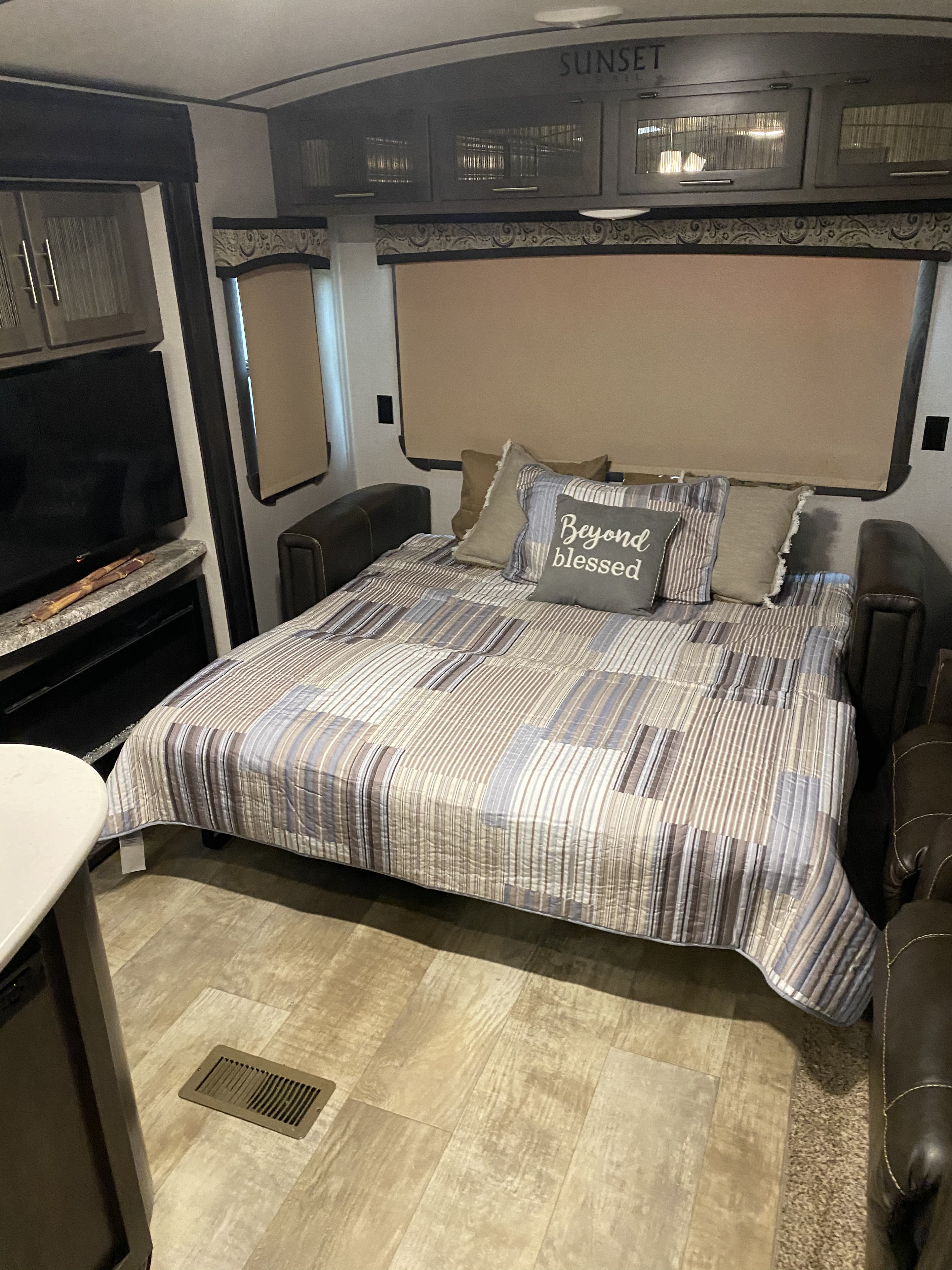 Cozy RV rental living area featuring a pull-out sofa bed with "Beyond Blessed" pillow, TV, and overhead "Sunset" cabinets.. Crossroads Sunset Trail Reserve 2018