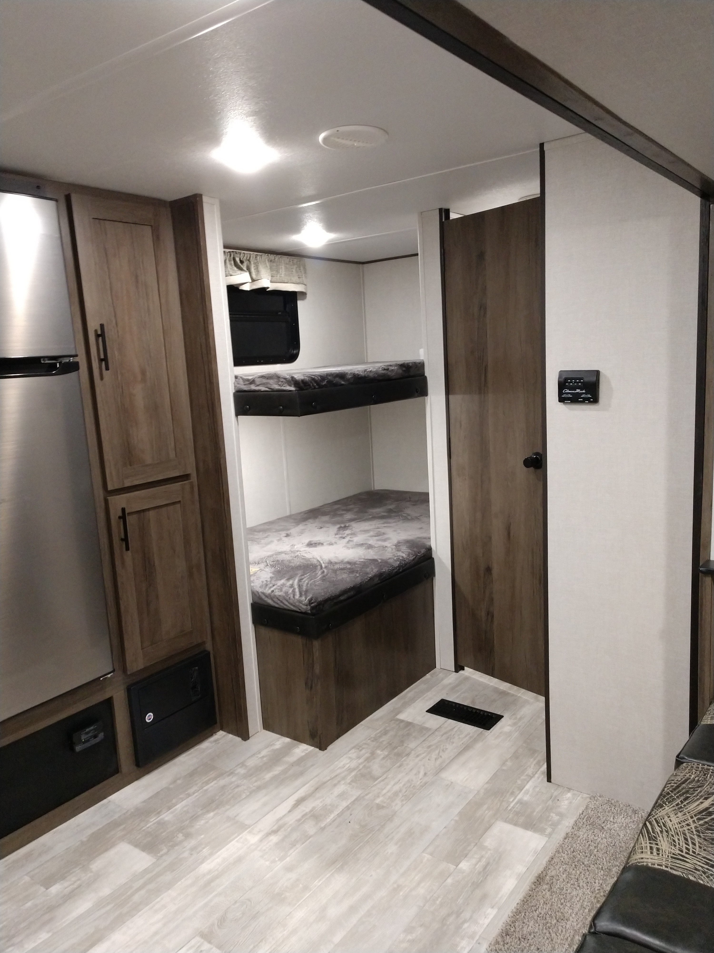 This RV rental interior features modern wood cabinetry, a stainless steel fridge, light flooring, and cozy bunk beds.. Prime Time Avenger 2021