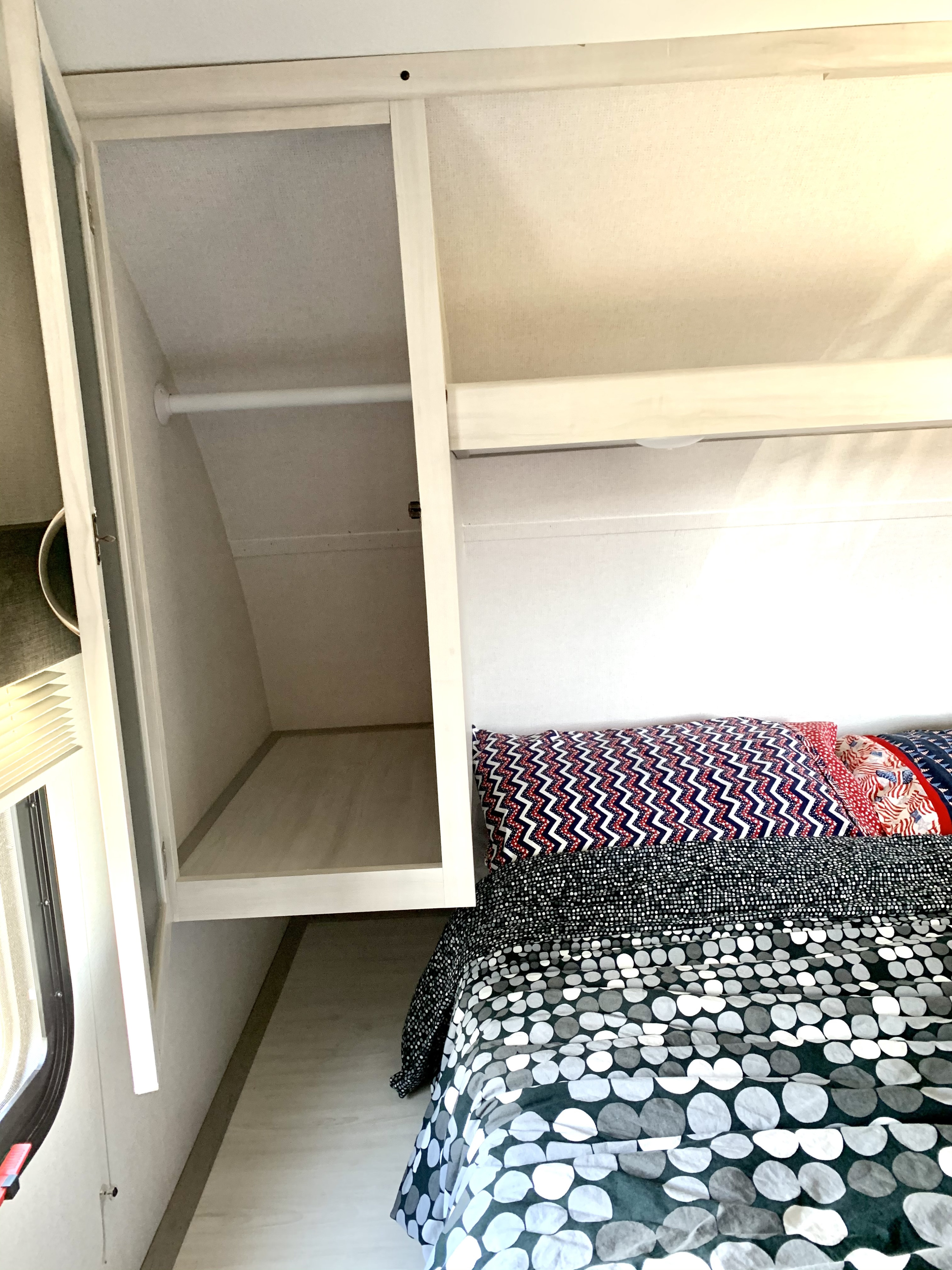 Compact RV rental bedroom featuring patterned bedding, open overhead storage, and a built-in closet.. Forest River Tracer 260BHSLE 2021