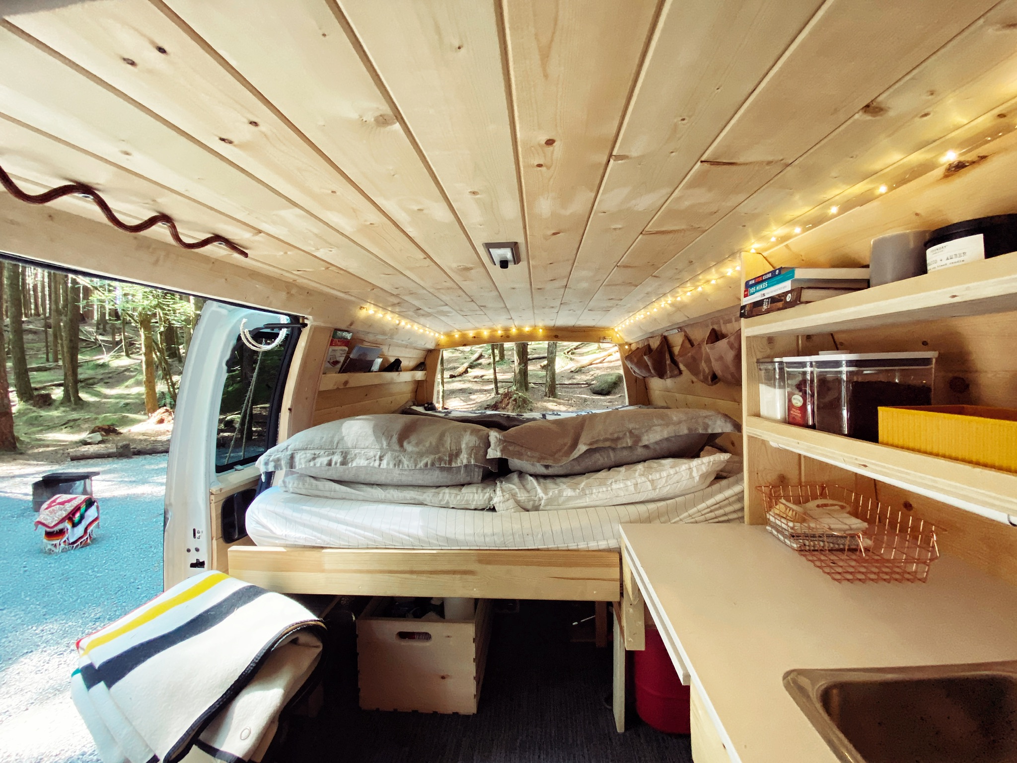 Inside a cozy RV rental: wood-clad camper van with comfy bed, compact kitchen, and scenic nature views. Ideal for adventure travel.. Chevrolet Express 2004