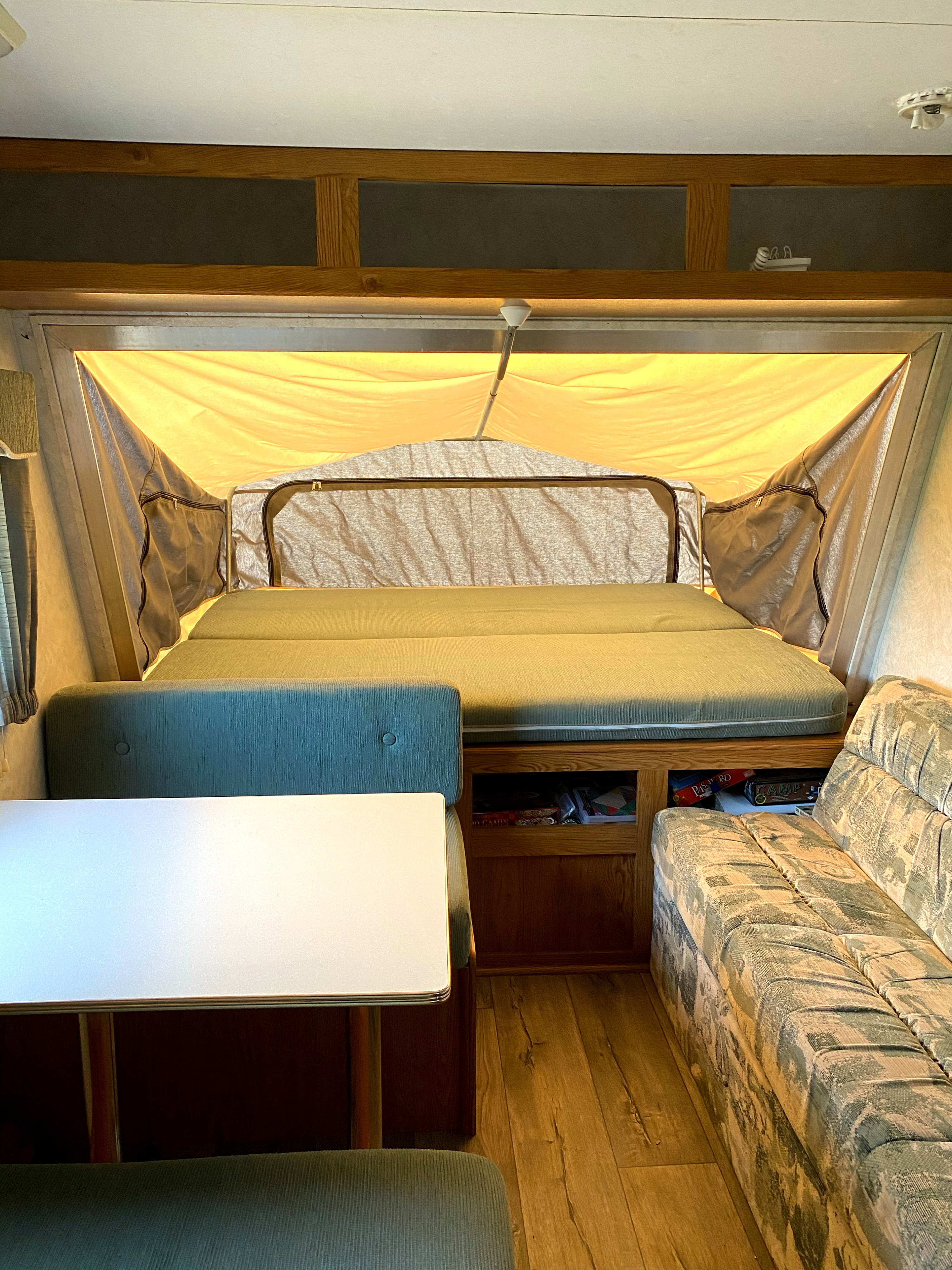 Cozy interior of an RV rental: a bright pop-up camper featuring a bed, dining area, couch, and wood accents.. Sportsmen Coyote 2001