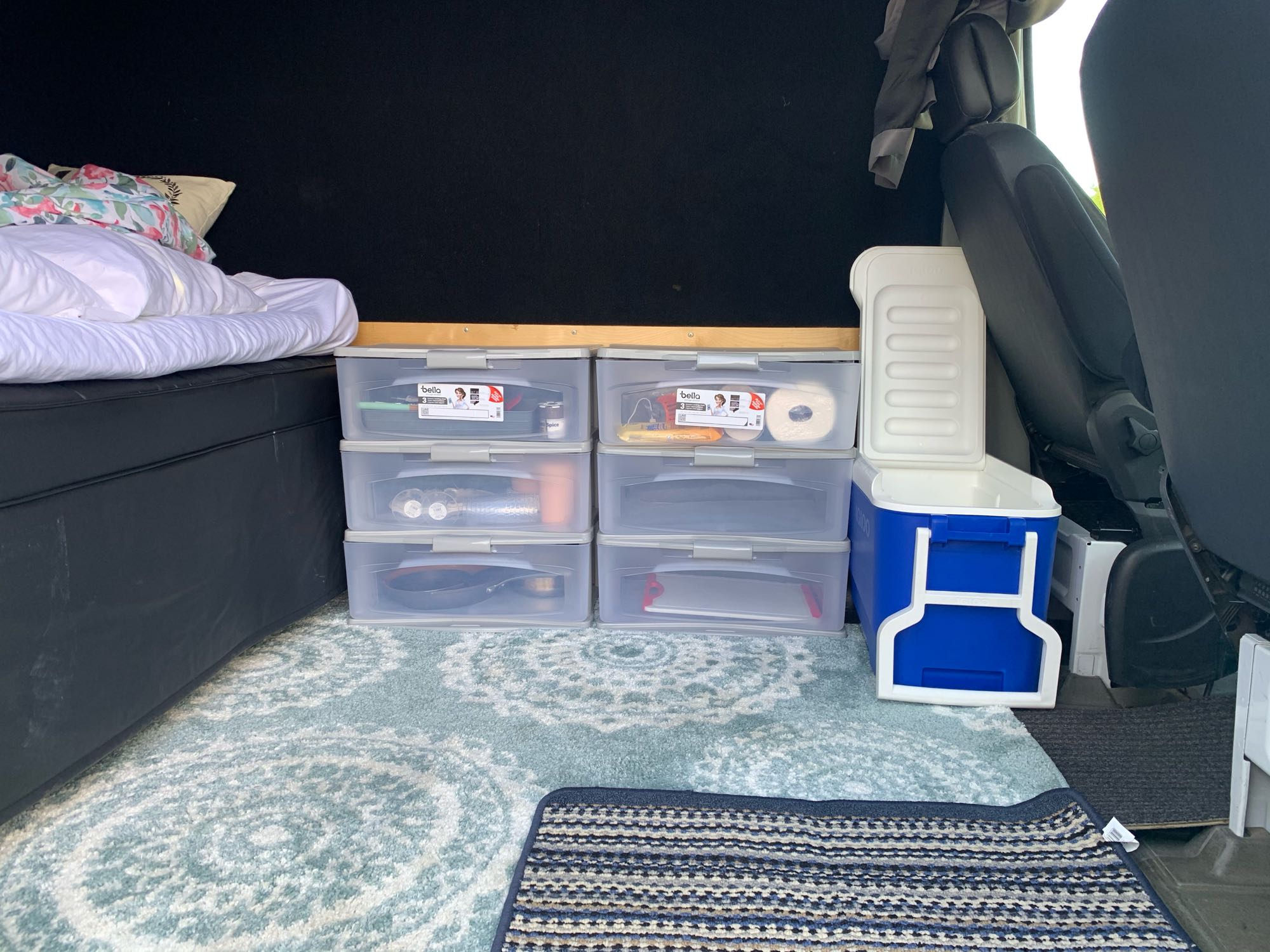 An organized RV rental interior with bed, clear storage bins for gear, coolers, and a comfy rug for travel.. Dodge Sprinter 2007