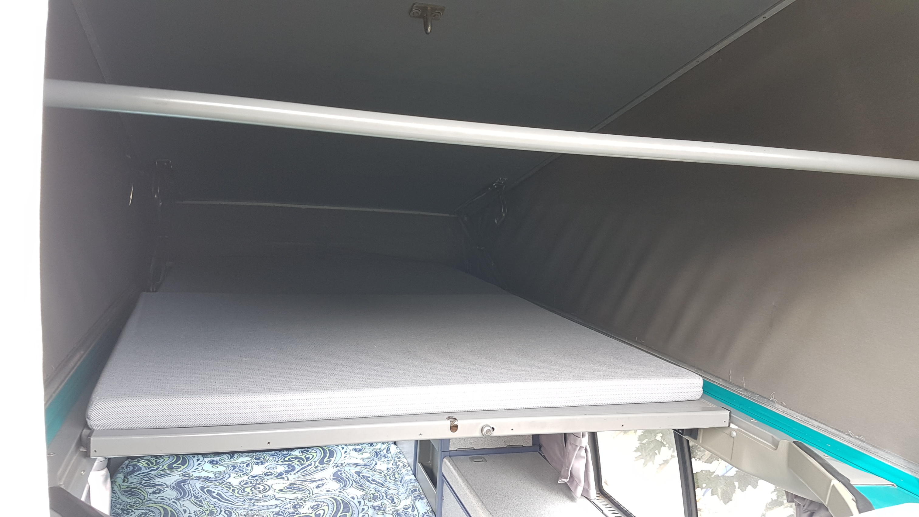Inside an RV rental, this pop-top sleeping area features a comfy grey mattress and overhead support bar, perfect for travel.. Volkswagen California - Westfalia 1996