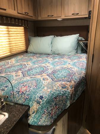 Cozy RV rental bedroom: comfy bed with a colorful quilt, pillows, and overhead wooden cabinets.. Coachmen Freelander 2018