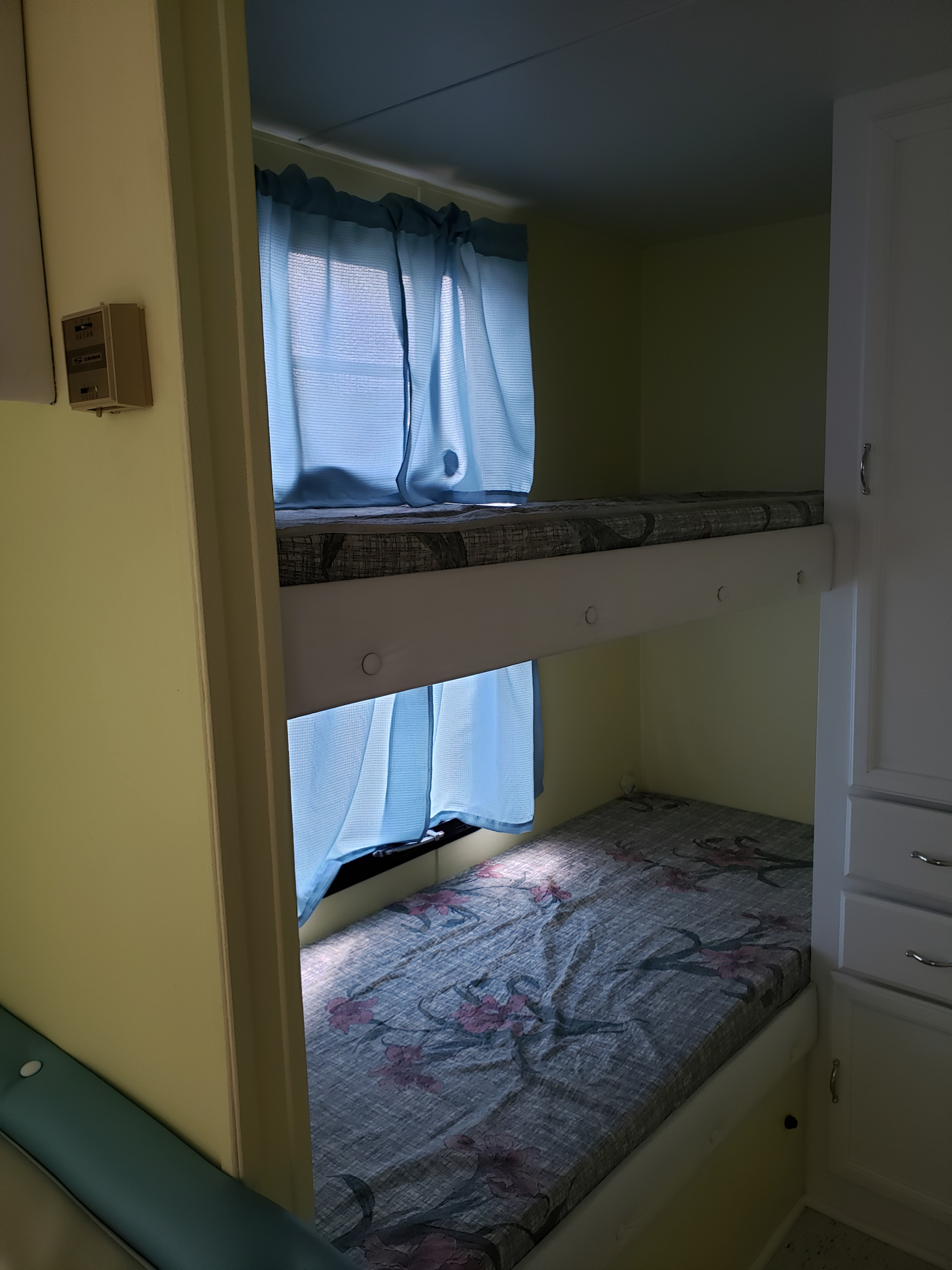 Cozy RV rental interior featuring two bunk beds with floral mattresses and blue window curtains.. Forest River Salem 1998